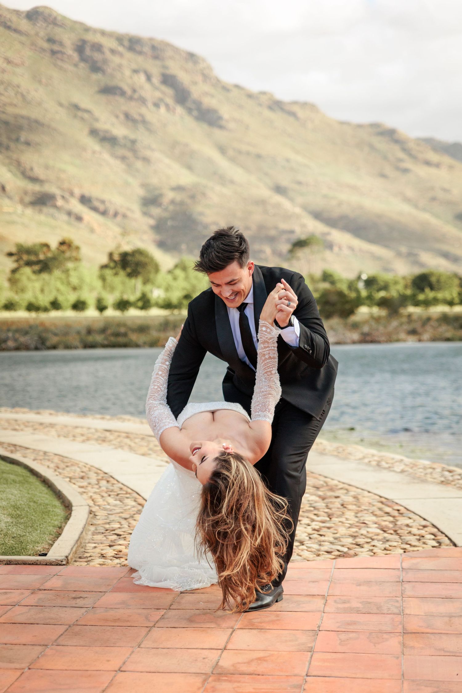 A couple in formal attire dances and dips romantically by a scenic mountain lake.