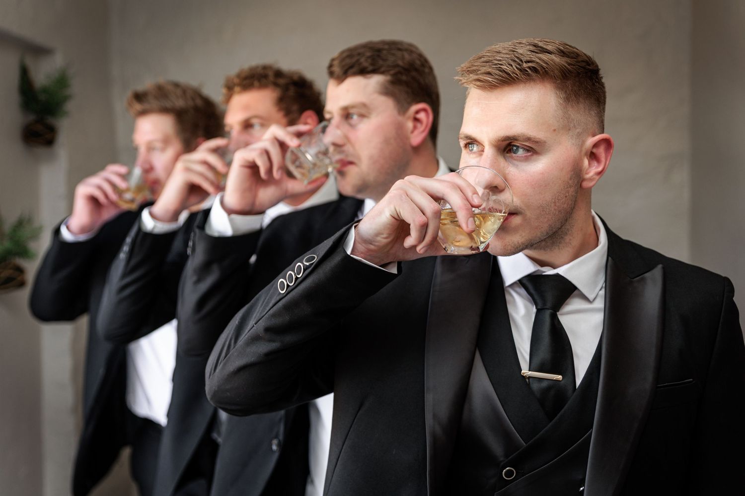 Groomsmen in black tuxedos and bowties stand in line while adjusting their bowties in a coordinated pose.
