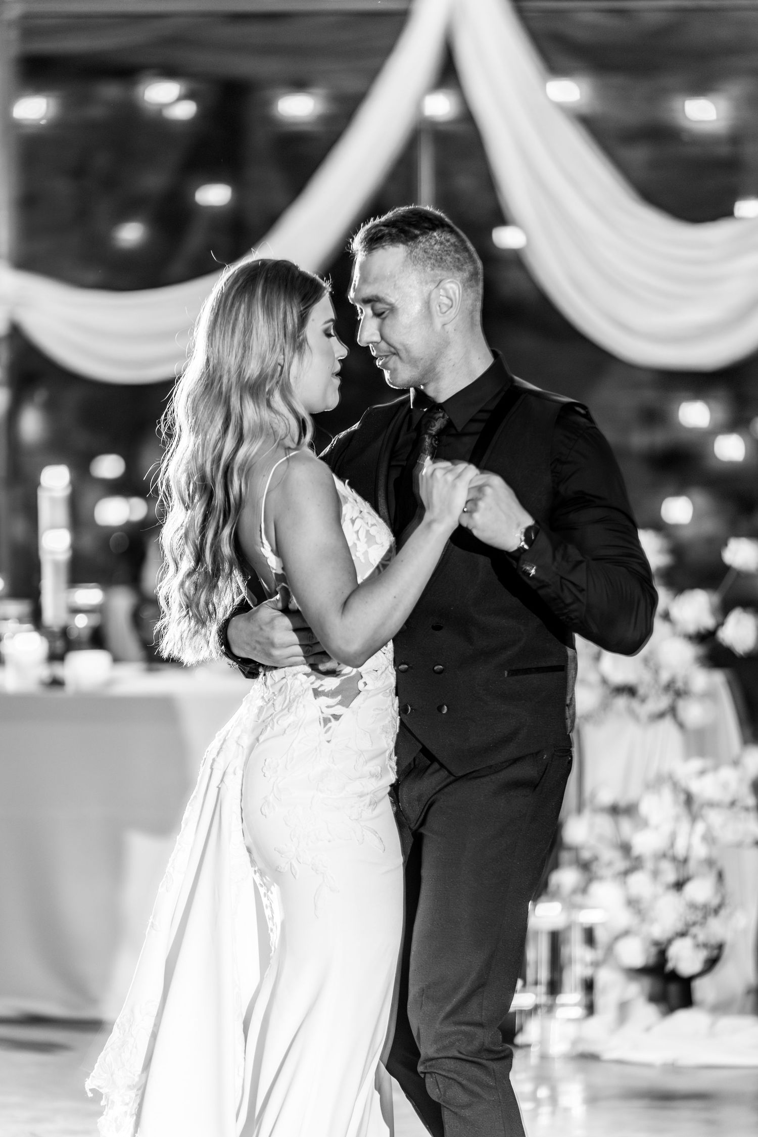 A romantic first dance sequence between newlyweds at a wedding reception with twinkling lights in the background.