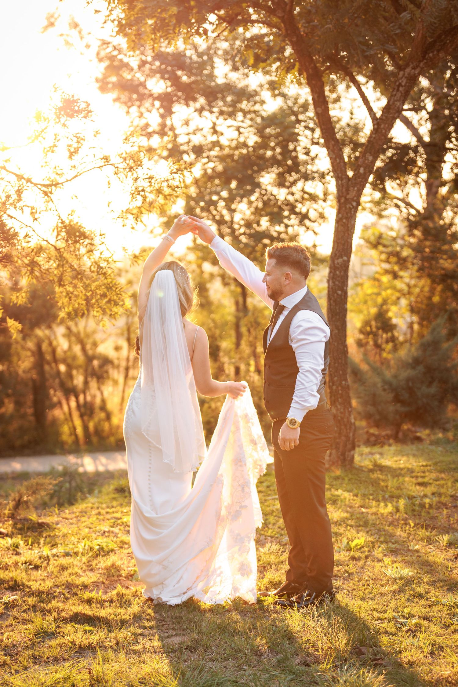 A couple shares a romantic moment at sunset in a golden-lit orchard with sunlight streaming through the trees.