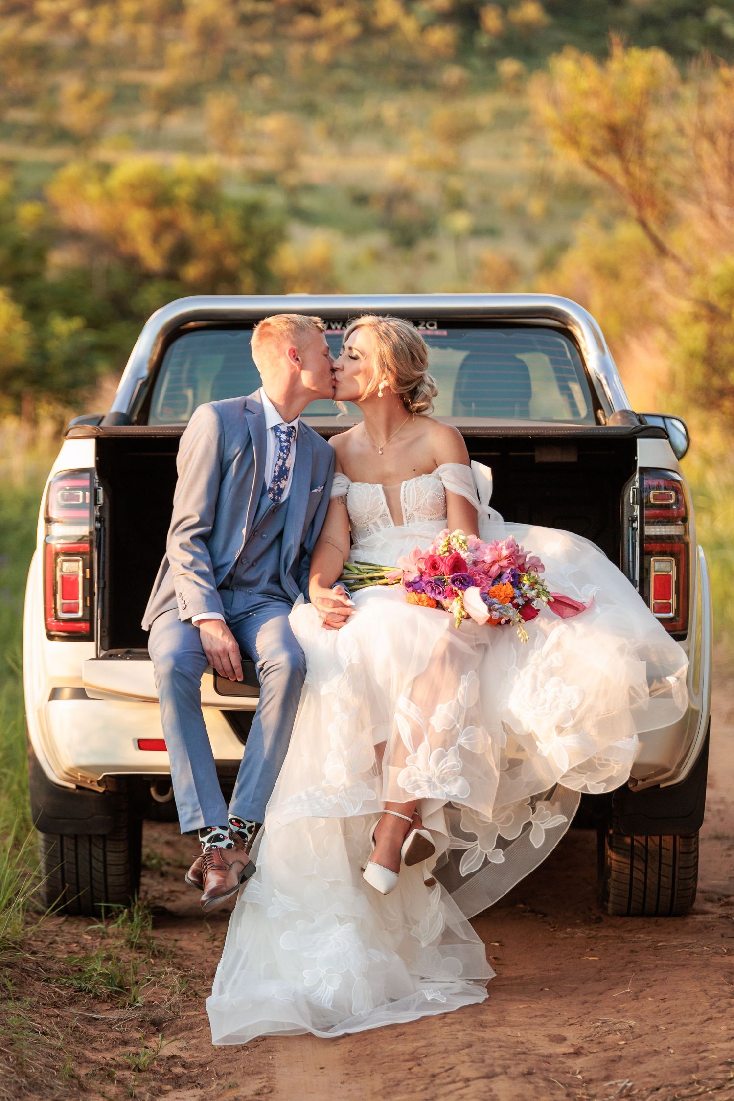 A romantic wedding photoshoot series showing a couple sitting in the back of a white pickup truck at sunset.