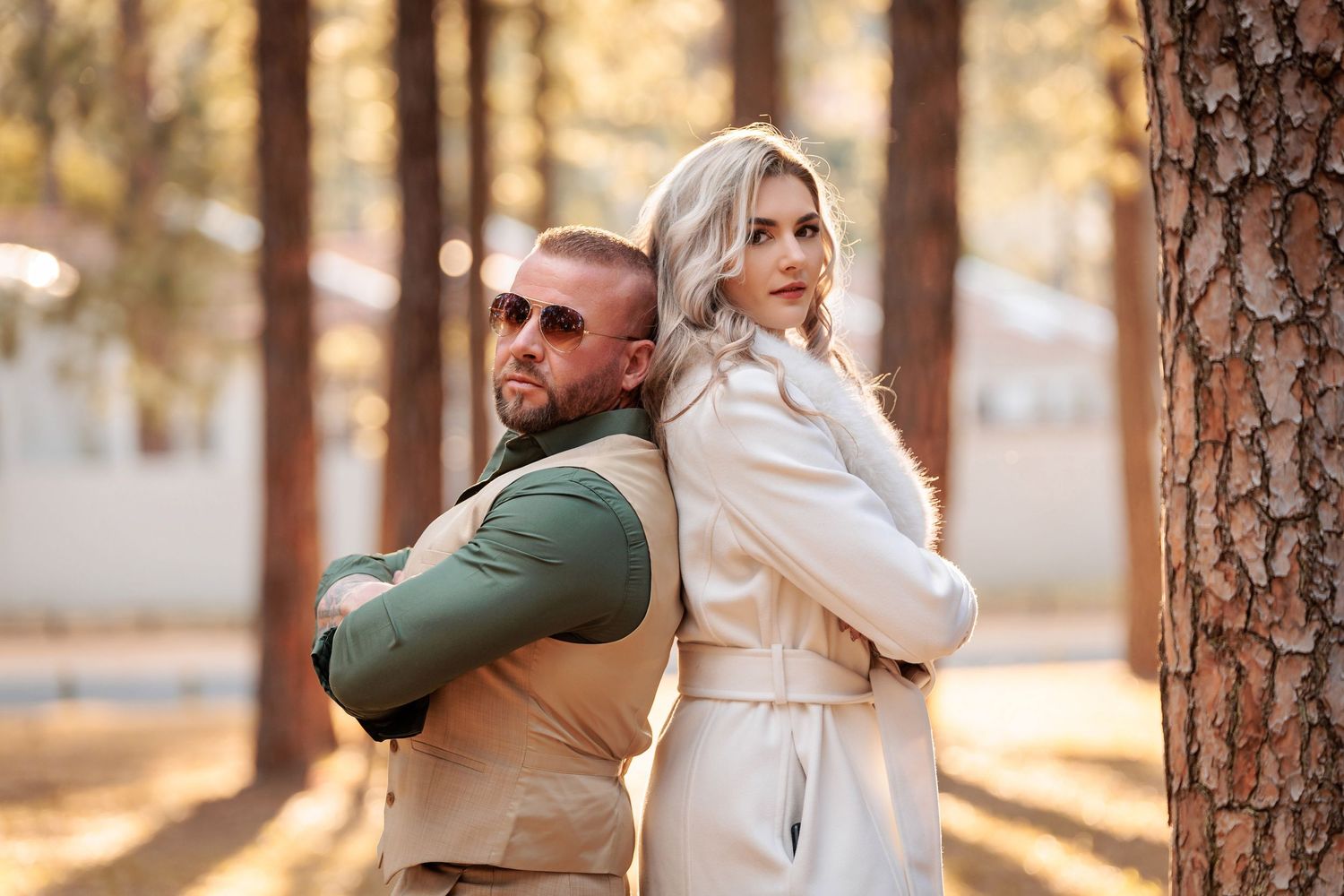 Romantic couple in winter coats embraces in a sunlit forest during golden hour.