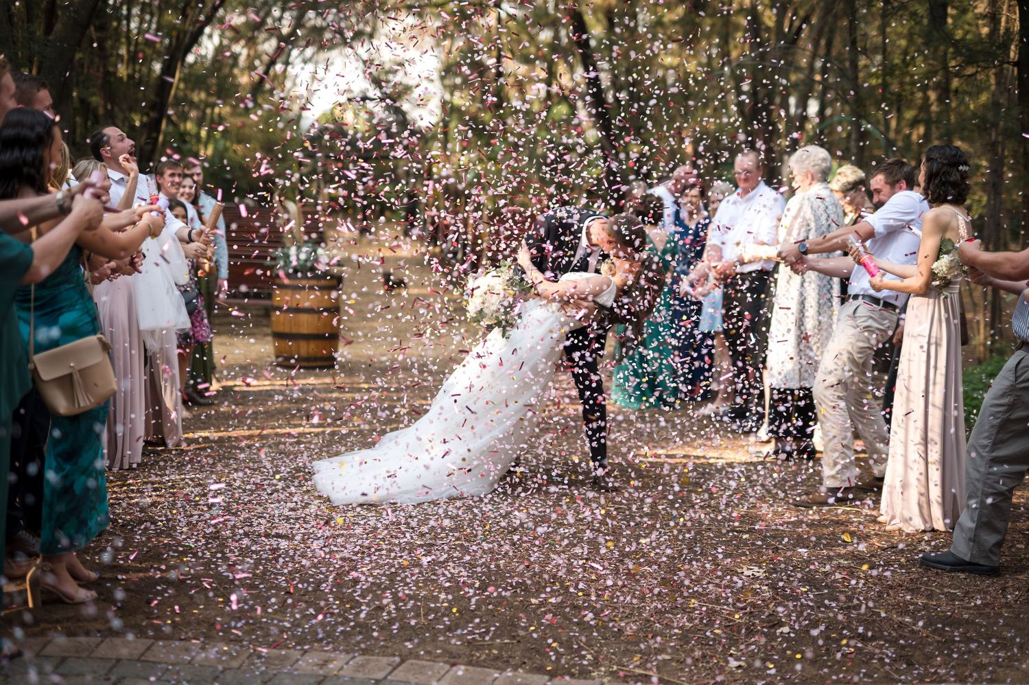 Wedding guests throw confetti during outdoor celebration.
