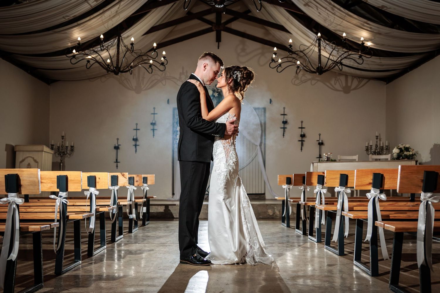 A couple shares an intimate moment in a church sanctuary with wooden pews and draped fabric decor.