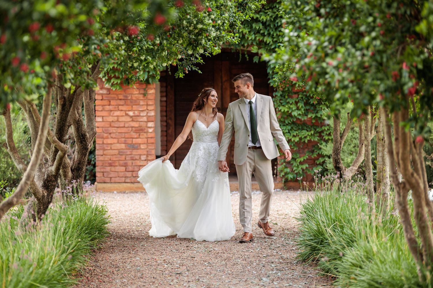 Newlyweds share an intimate moment on a brick-lined garden path surrounded by lush greenery.