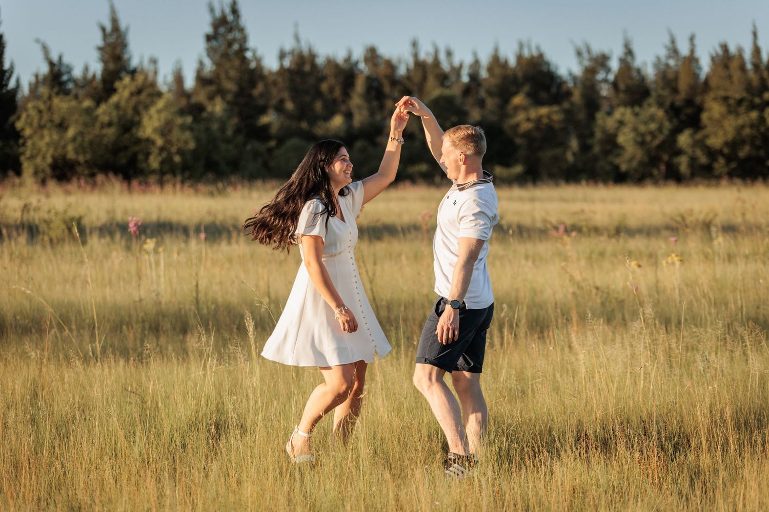 Two people walk through a golden field at sunset holding hands and enjoying a peaceful moment together.
