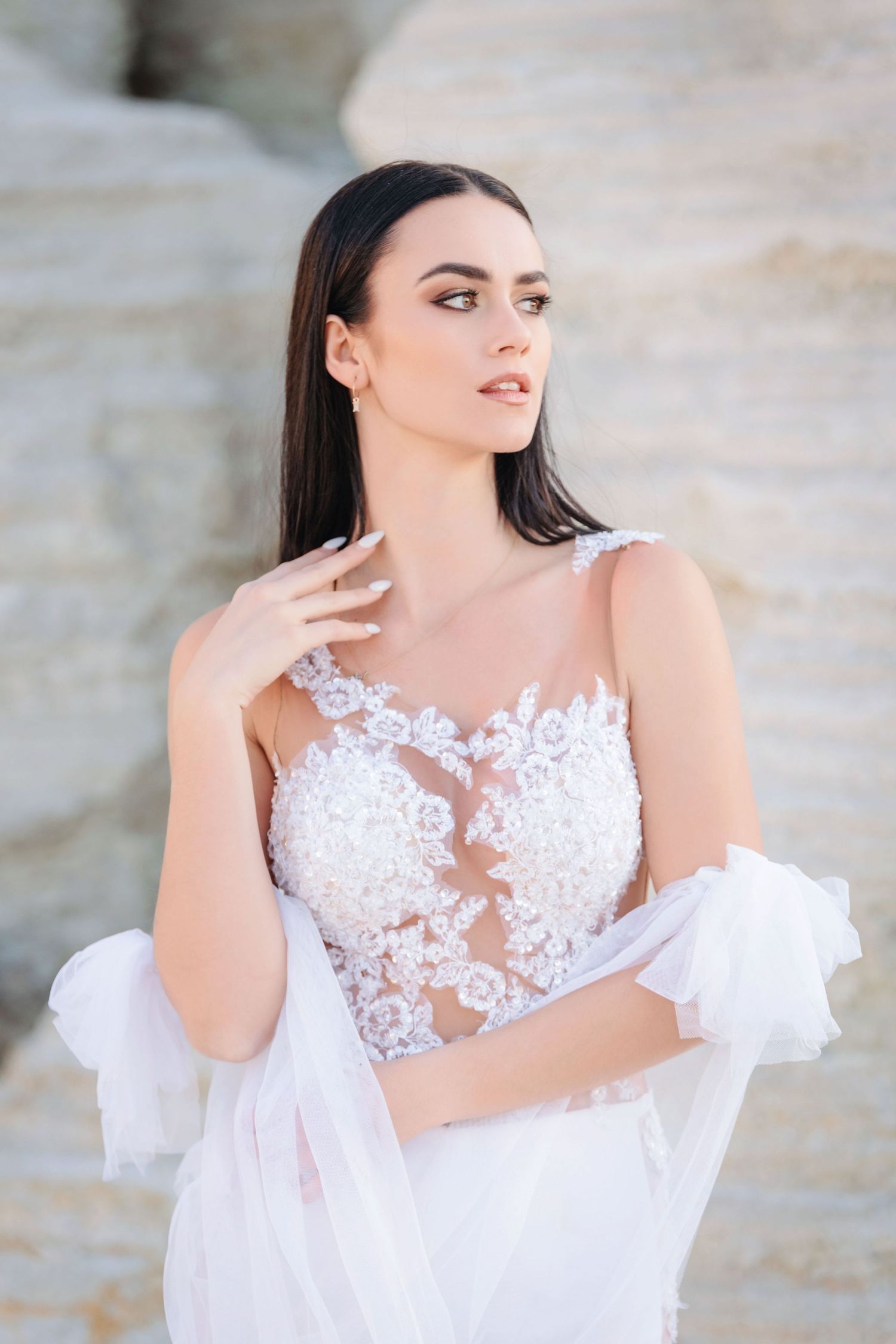 Bride in elegant white lace wedding dress with sheer details poses gracefully in outdoor portrait series.