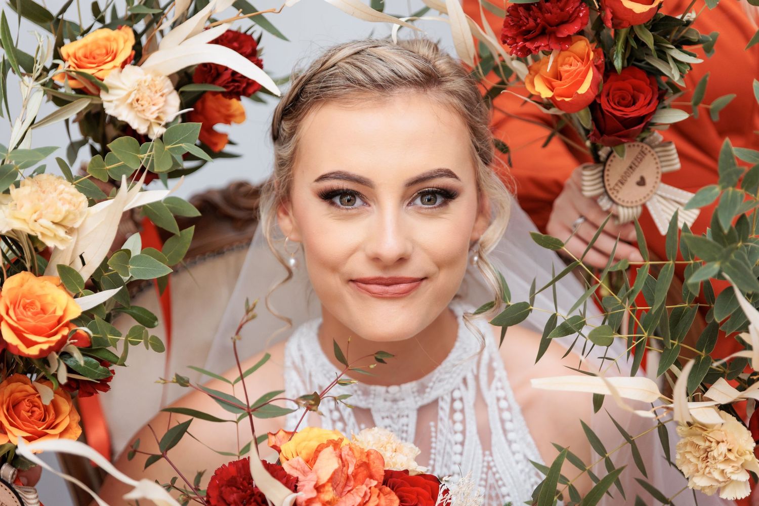 A bridal portrait framed by vibrant orange and peach floral arrangements.