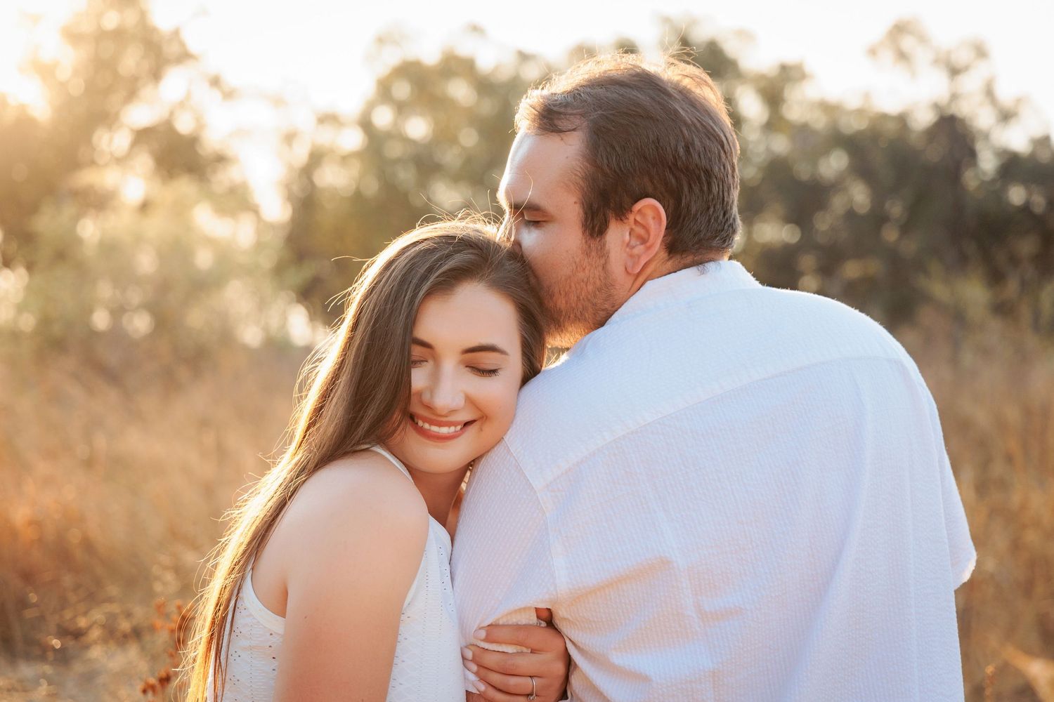 A couple embraces during a golden hour photoshoot in a field at sunset.