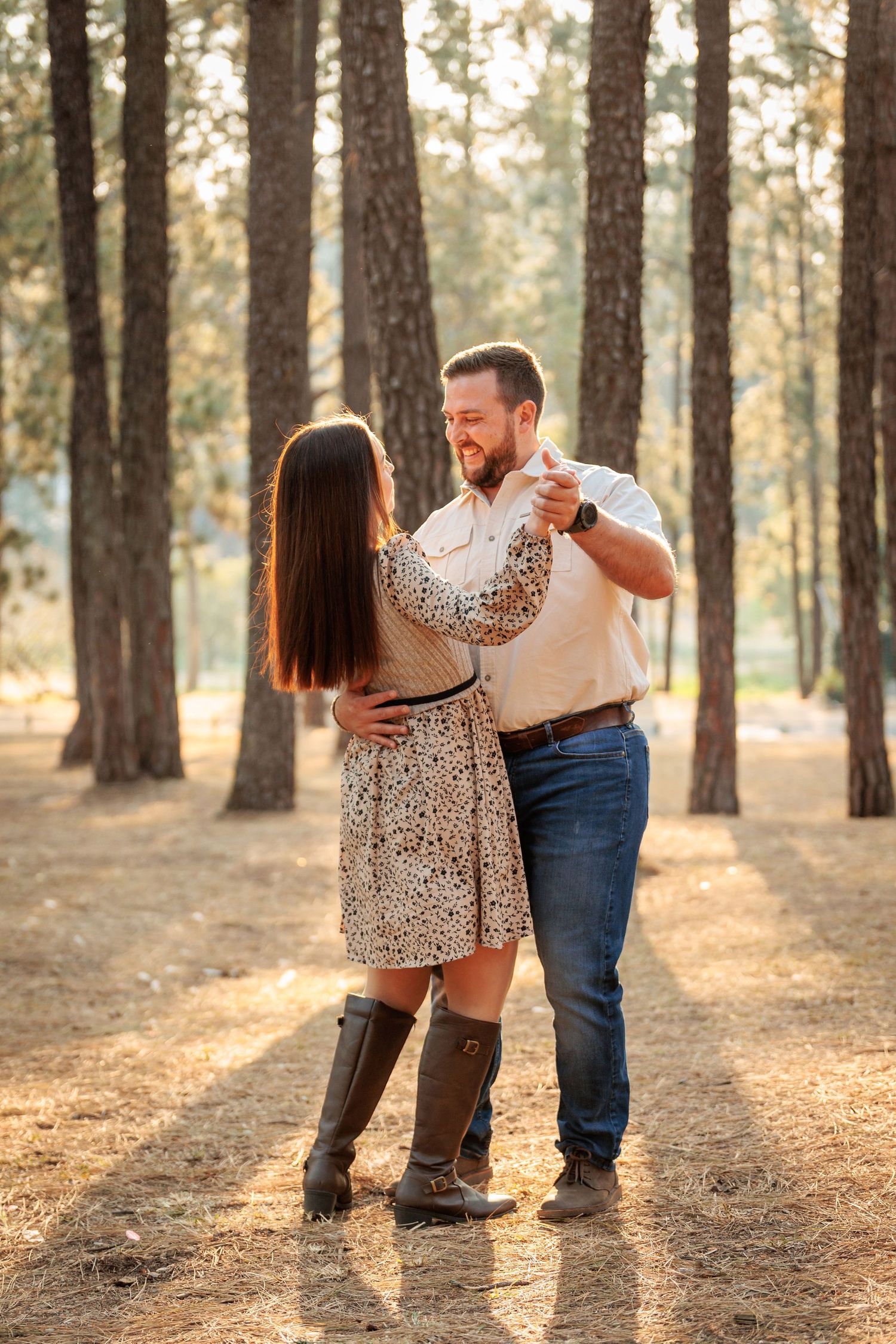 A couple dances together in a sunlit forest with tall pine trees during golden hour.