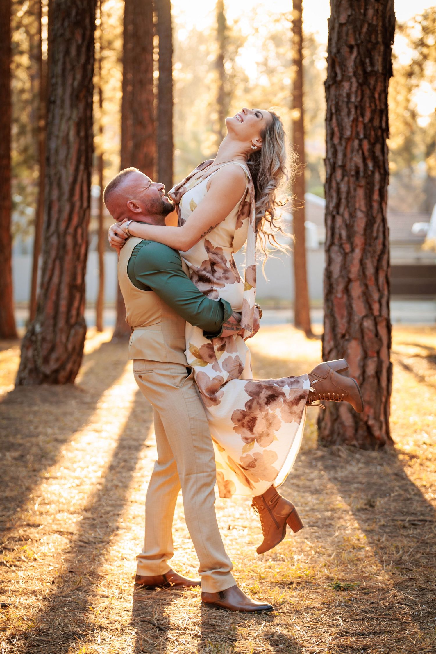 Couple embraces playfully in a sun-drenched pine forest during golden hour.