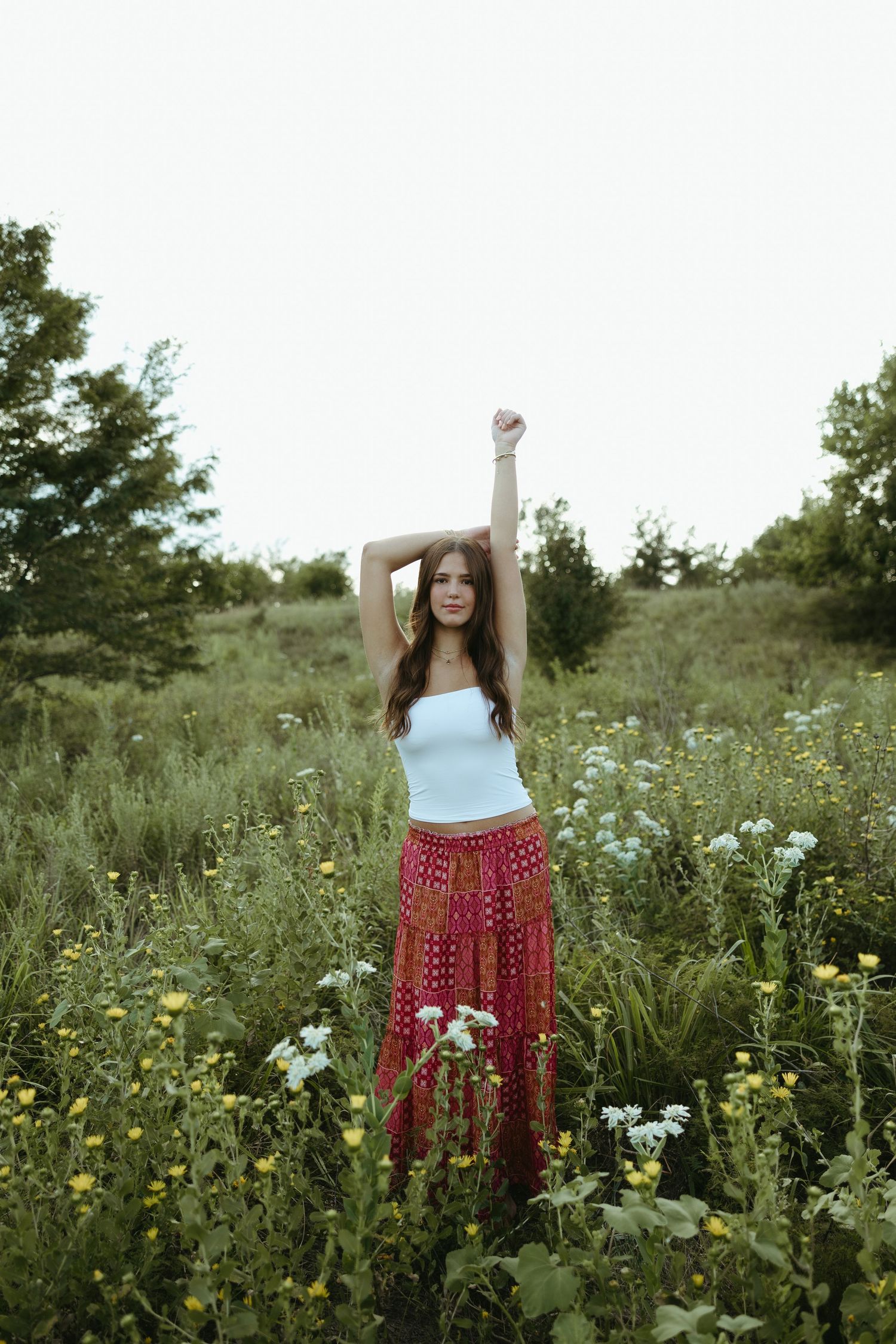 A joyful figure stretches in a wildflower meadow wearing a blue tank top and patterned red skirt.