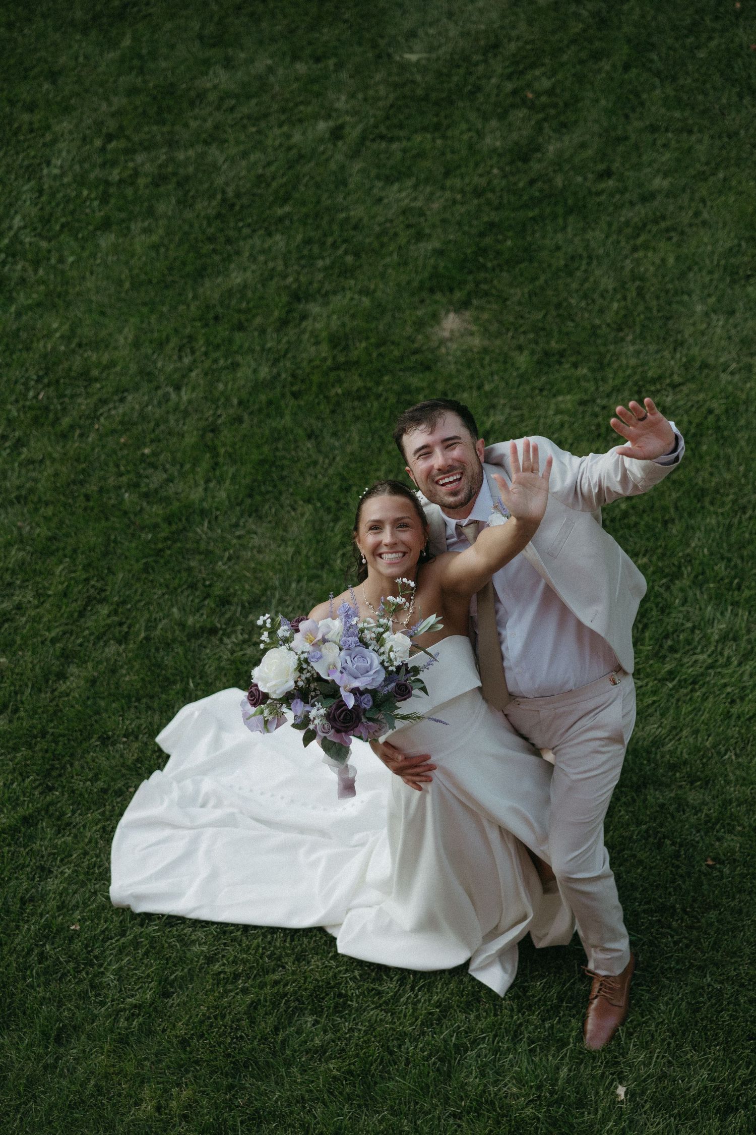 Newlyweds lay together on grass during outdoor wedding photoshoot.