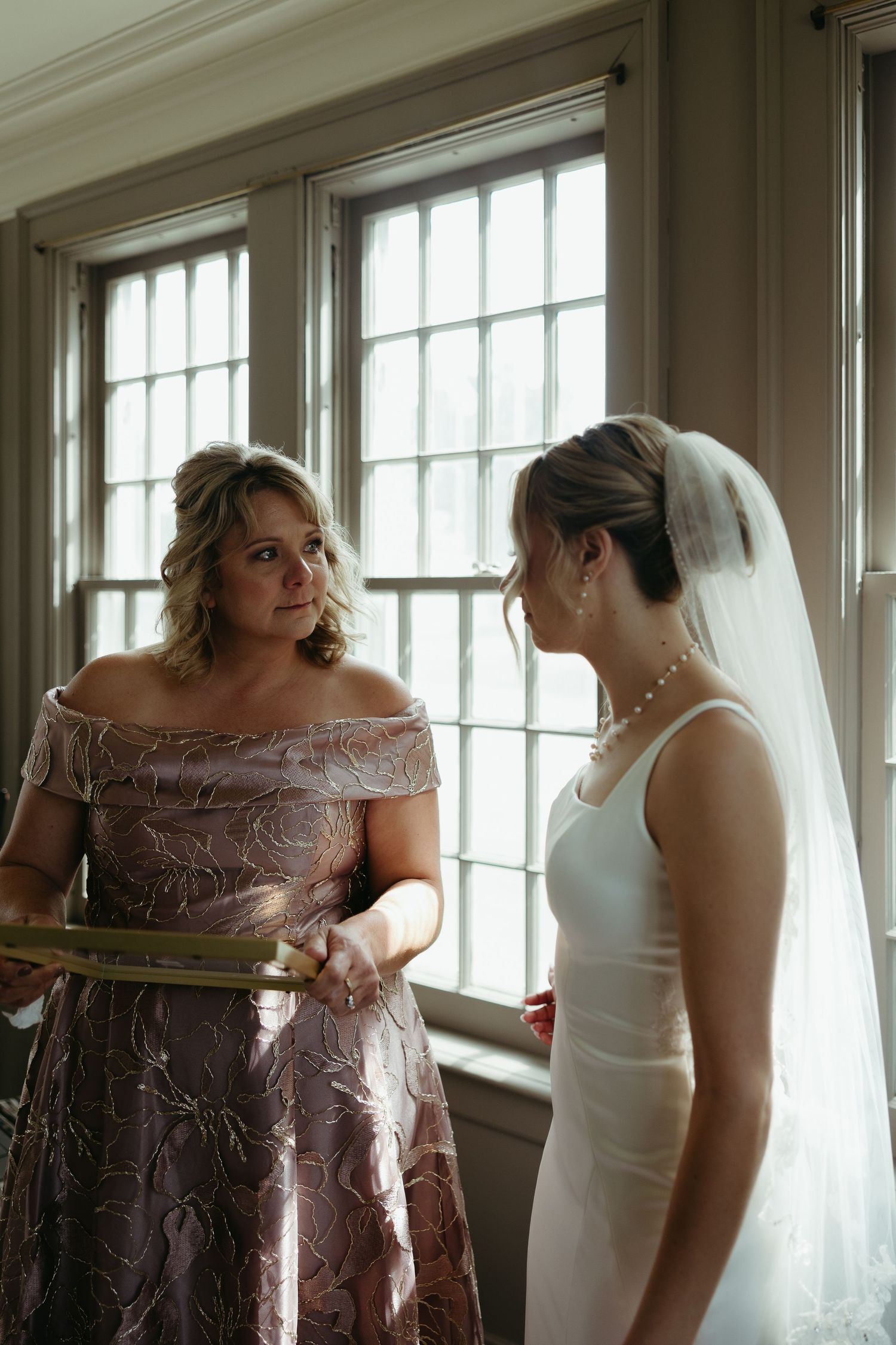 Wedding party helping with final dress preparations in a sunlit room.