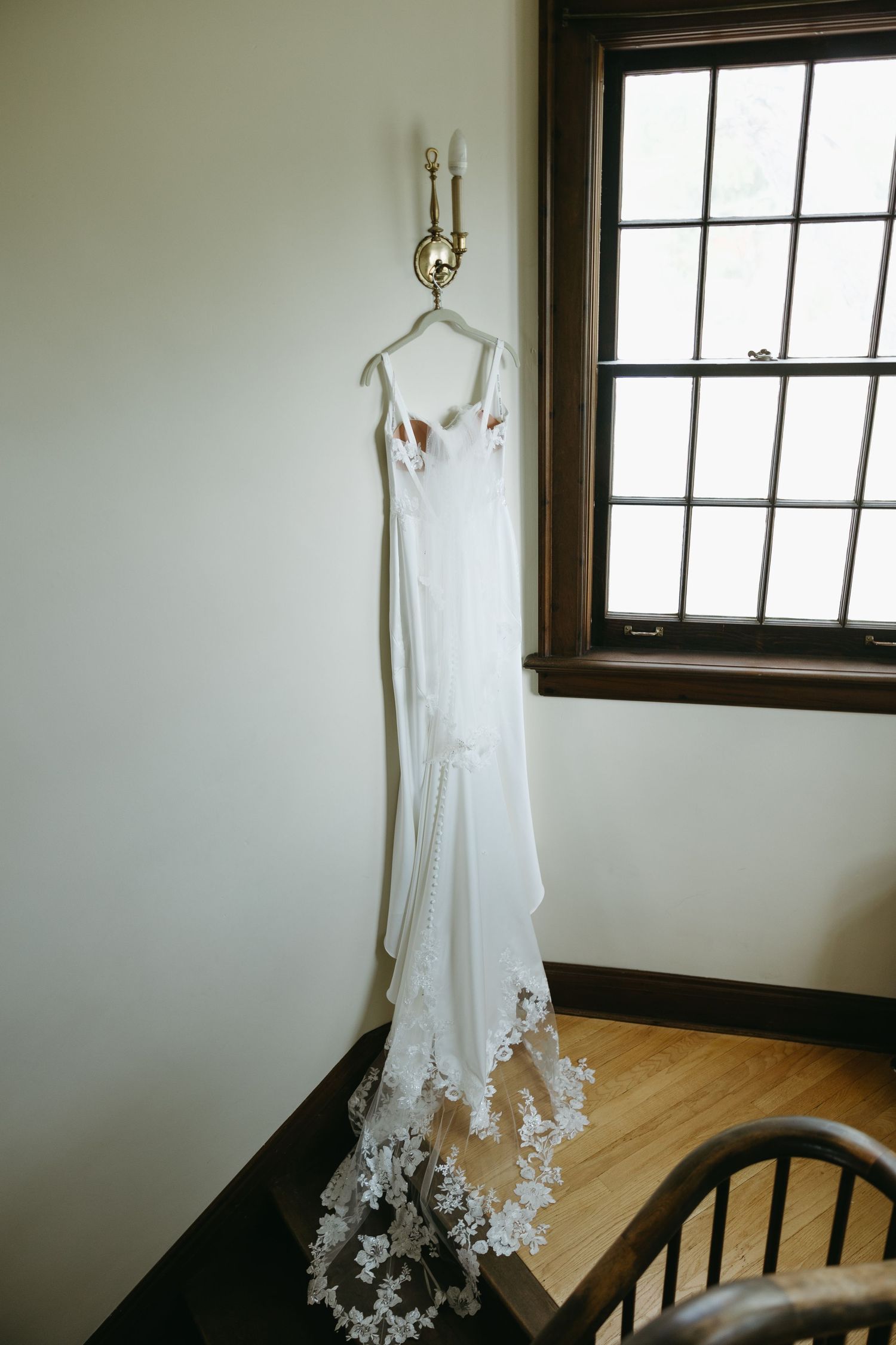 A white wedding dress with lace details displayed against a window in natural light.