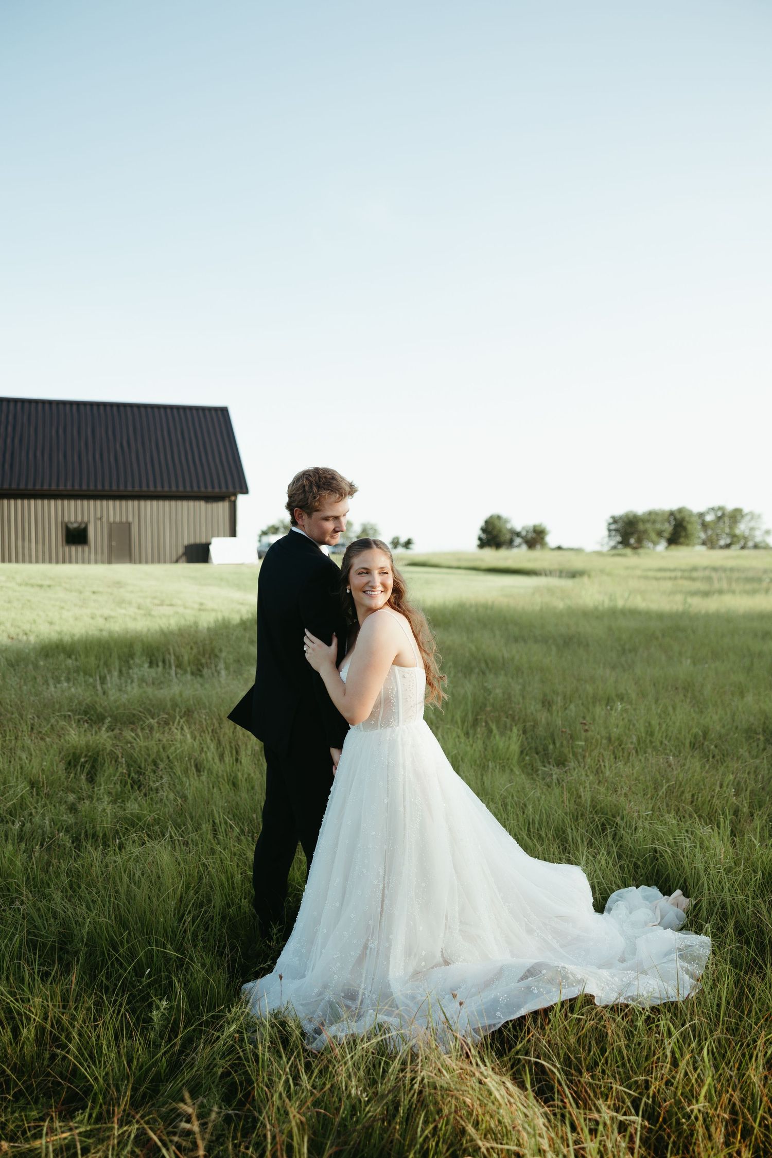Couple dances in an open field with a rustic barn in the background.
