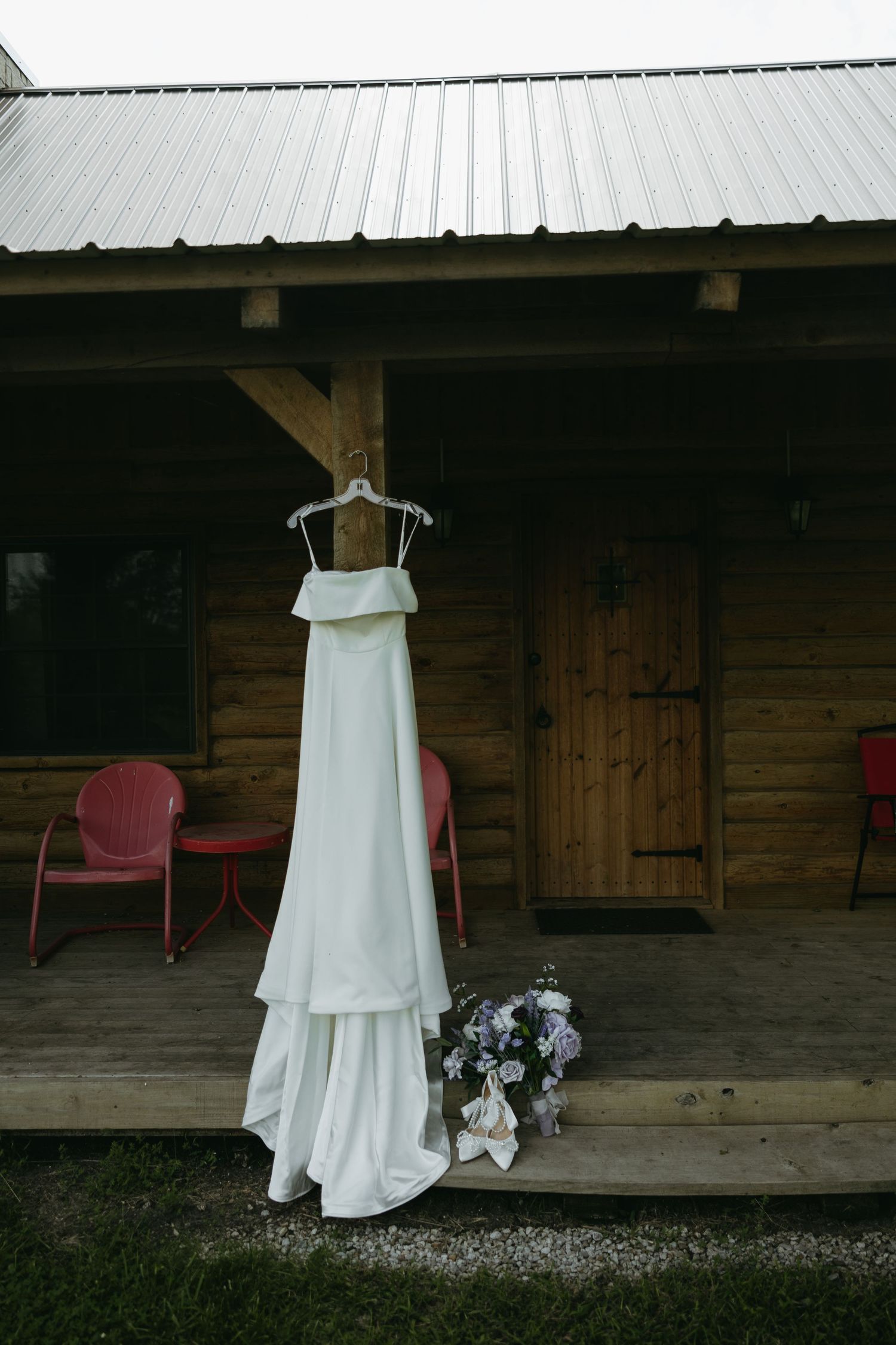 White wedding dress hangs on display against rustic wooden barn exterior.