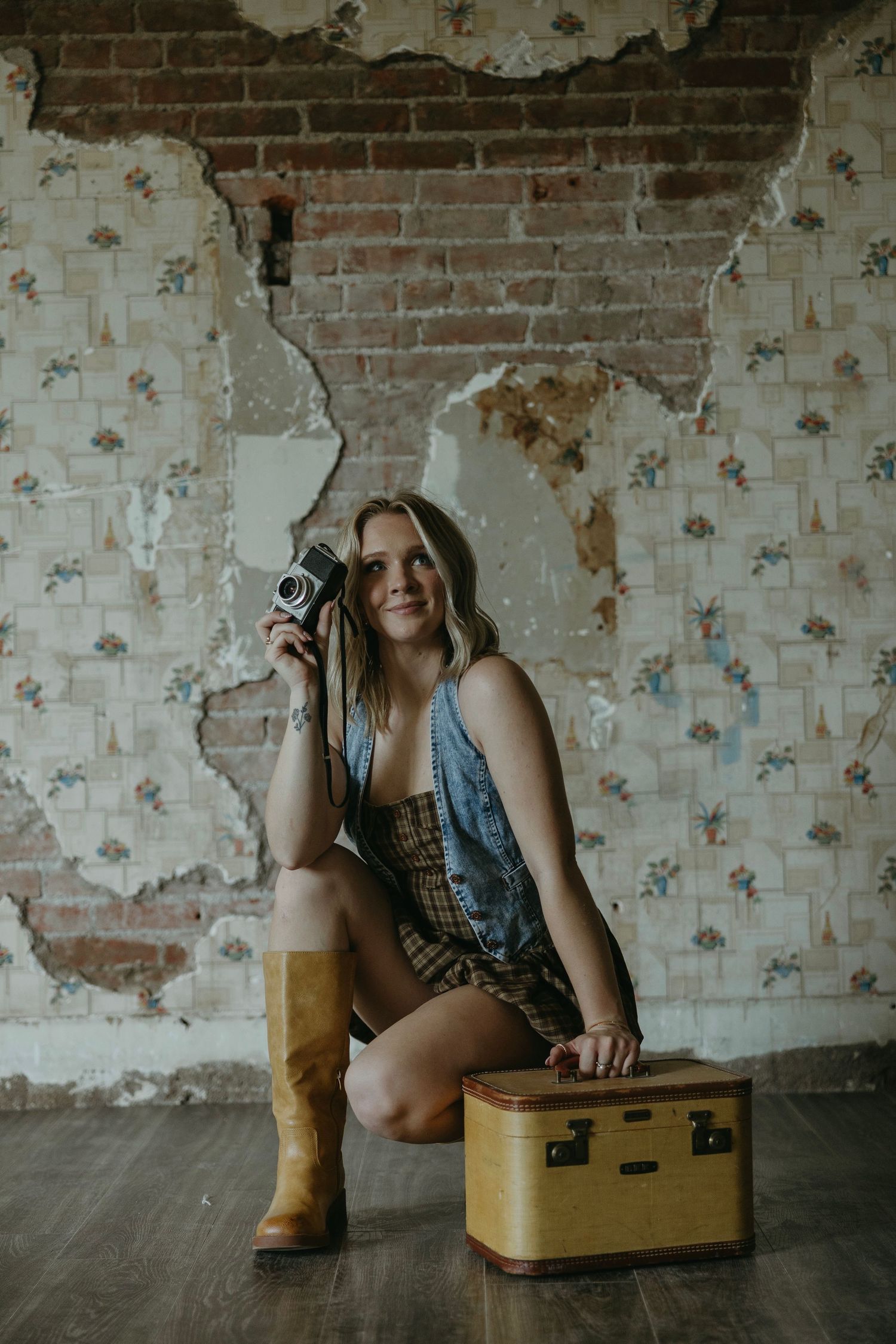 Artistic portrait session with vintage suitcase against weathered brick wall background.