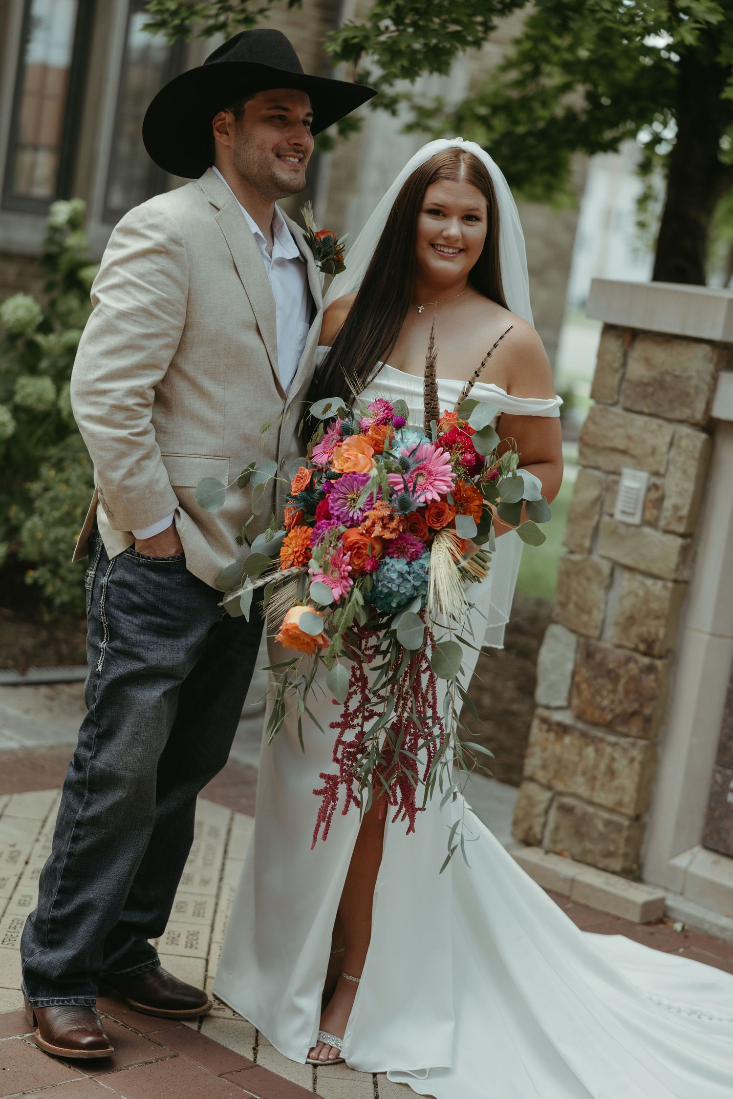 Couple in western wedding attire poses with vibrant colorful bouquet.