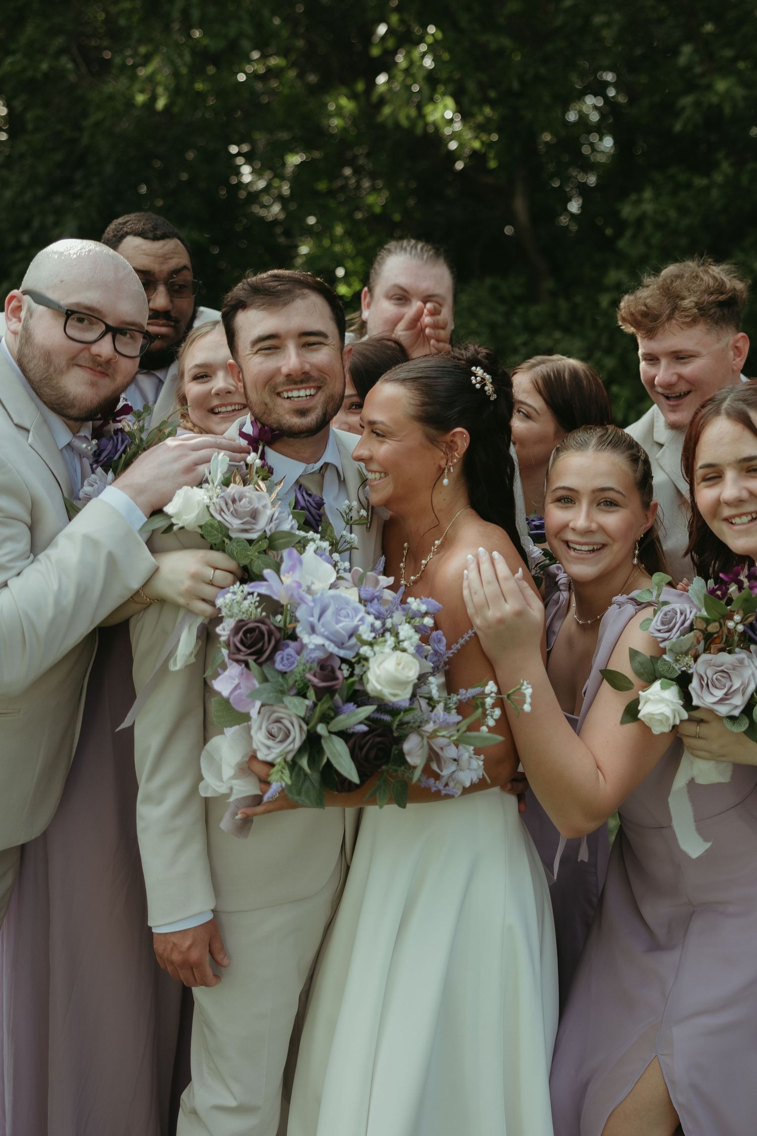 Wedding party in lavender and beige poses together with purple and white bouquets.