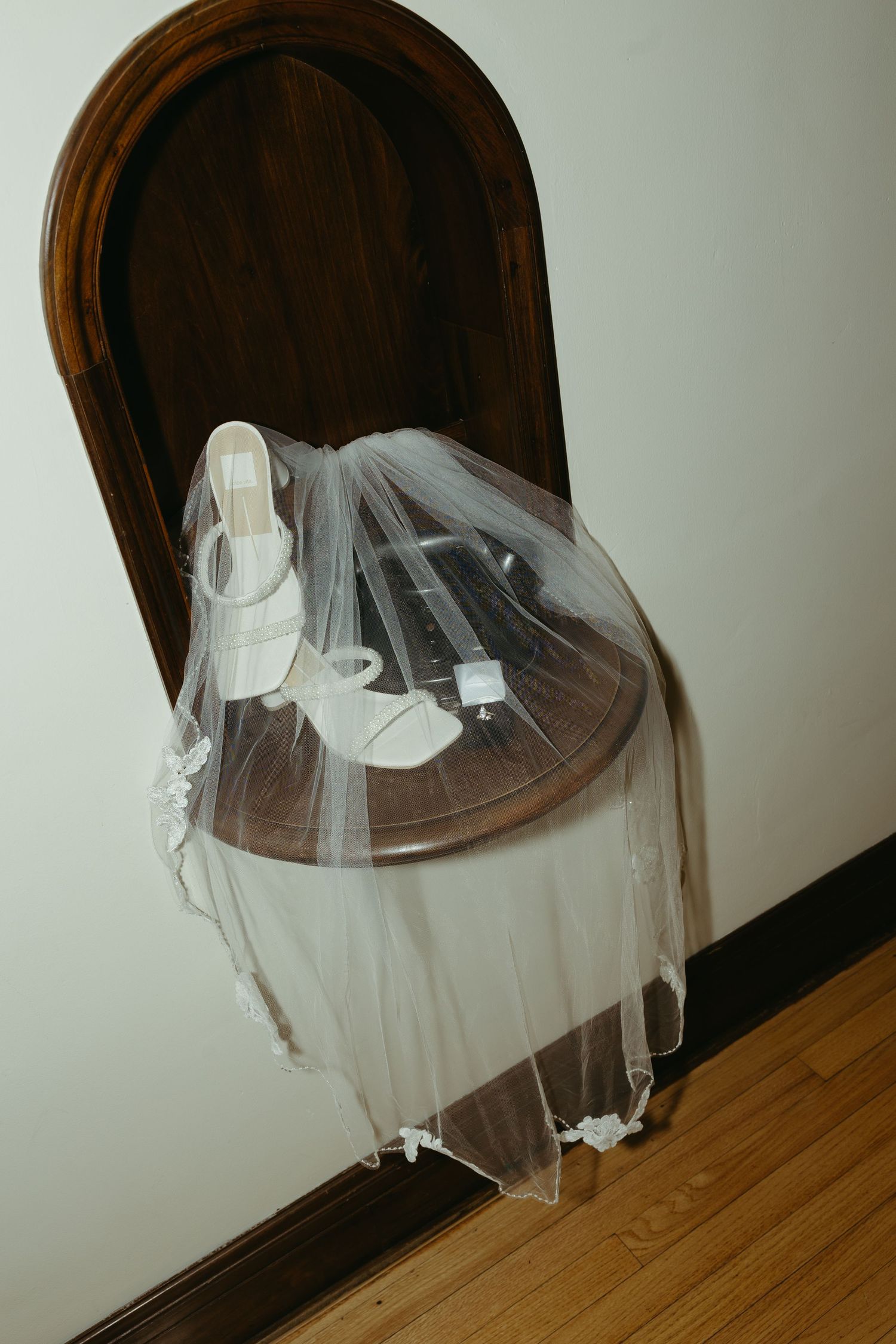 A delicate white wedding veil hangs elegantly against a dark wooden door.