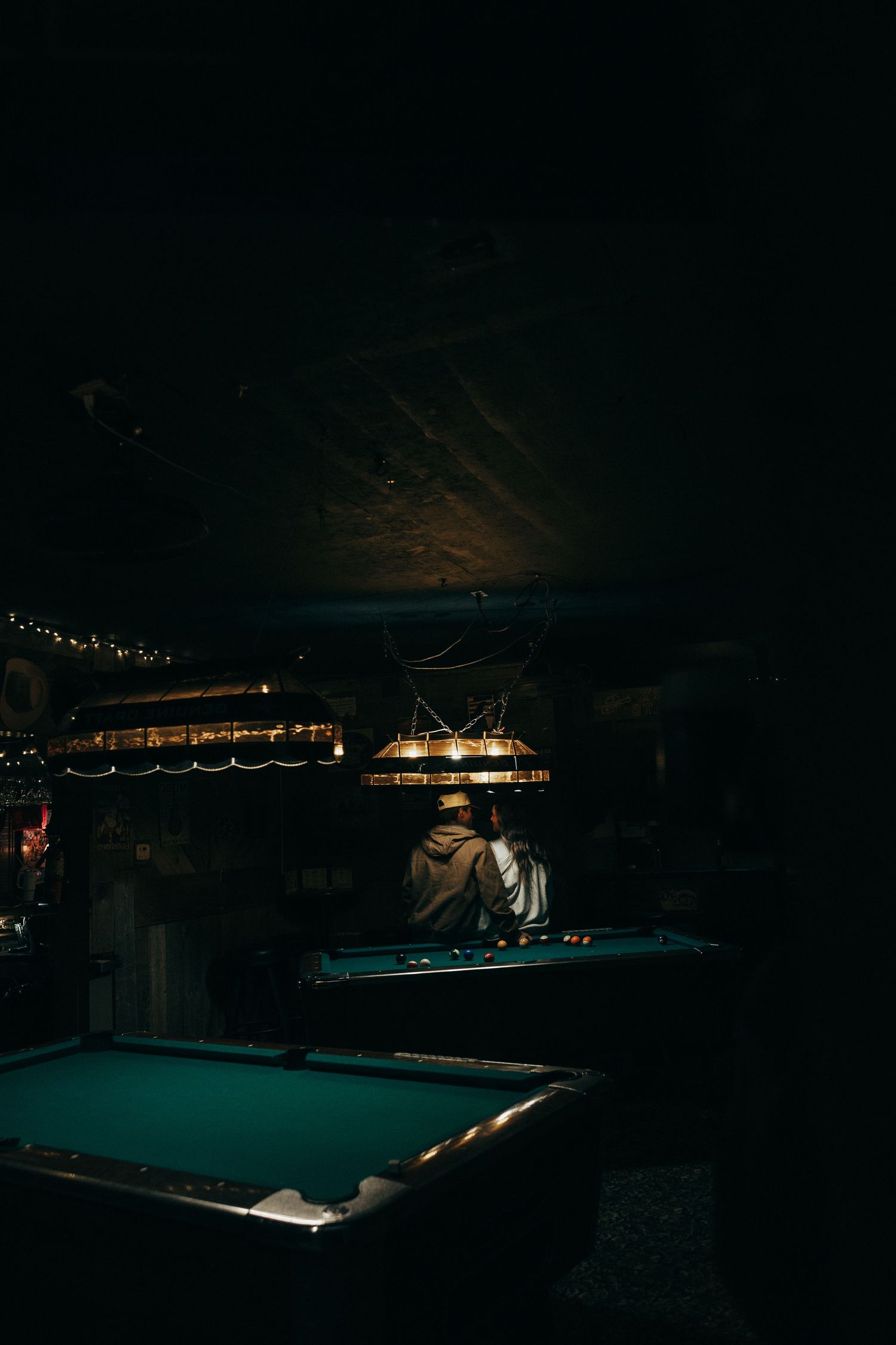 Pool tables illuminated by hanging lights in a dimly lit room.