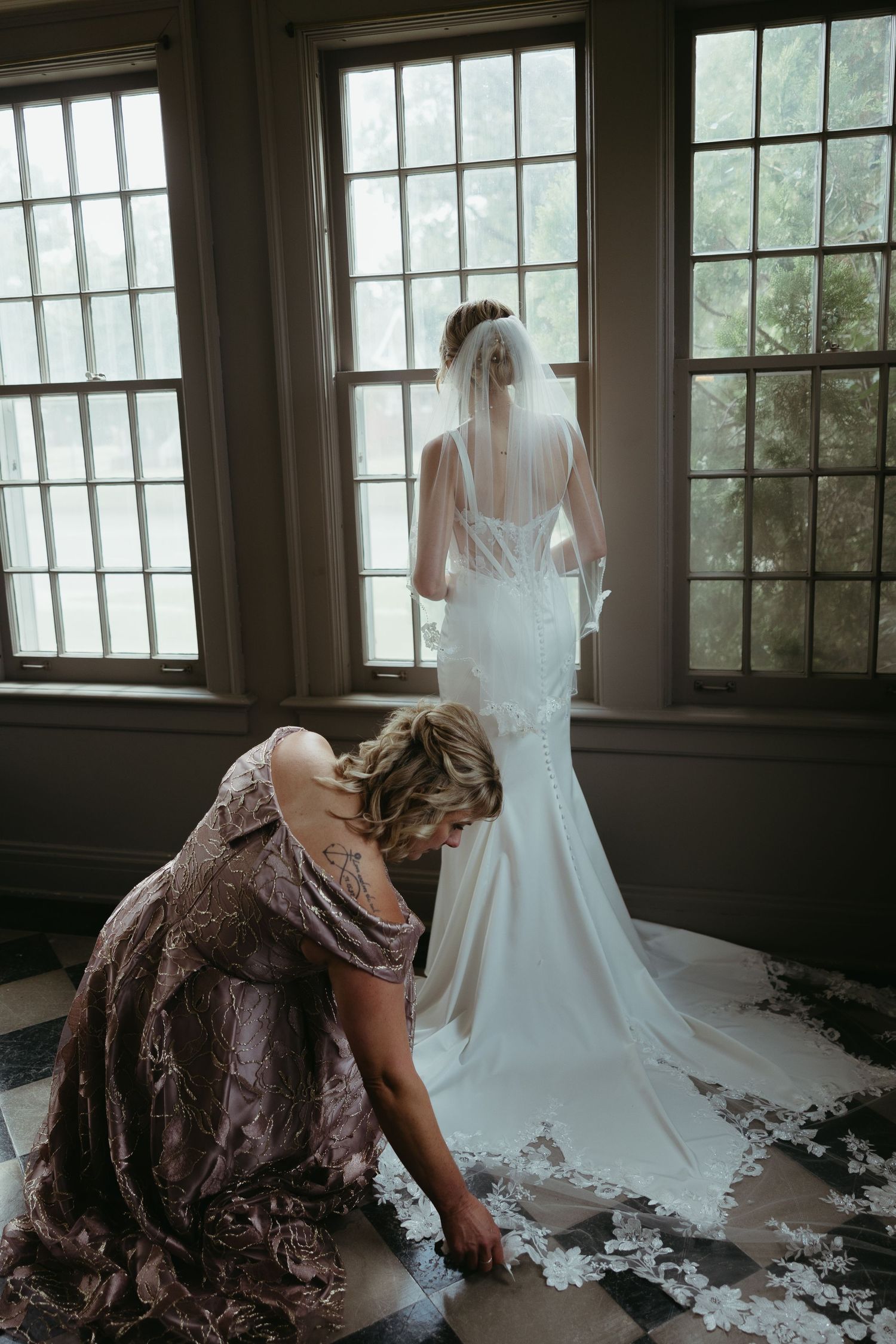 Wedding dress train with intricate lace details spread across checkered floor.