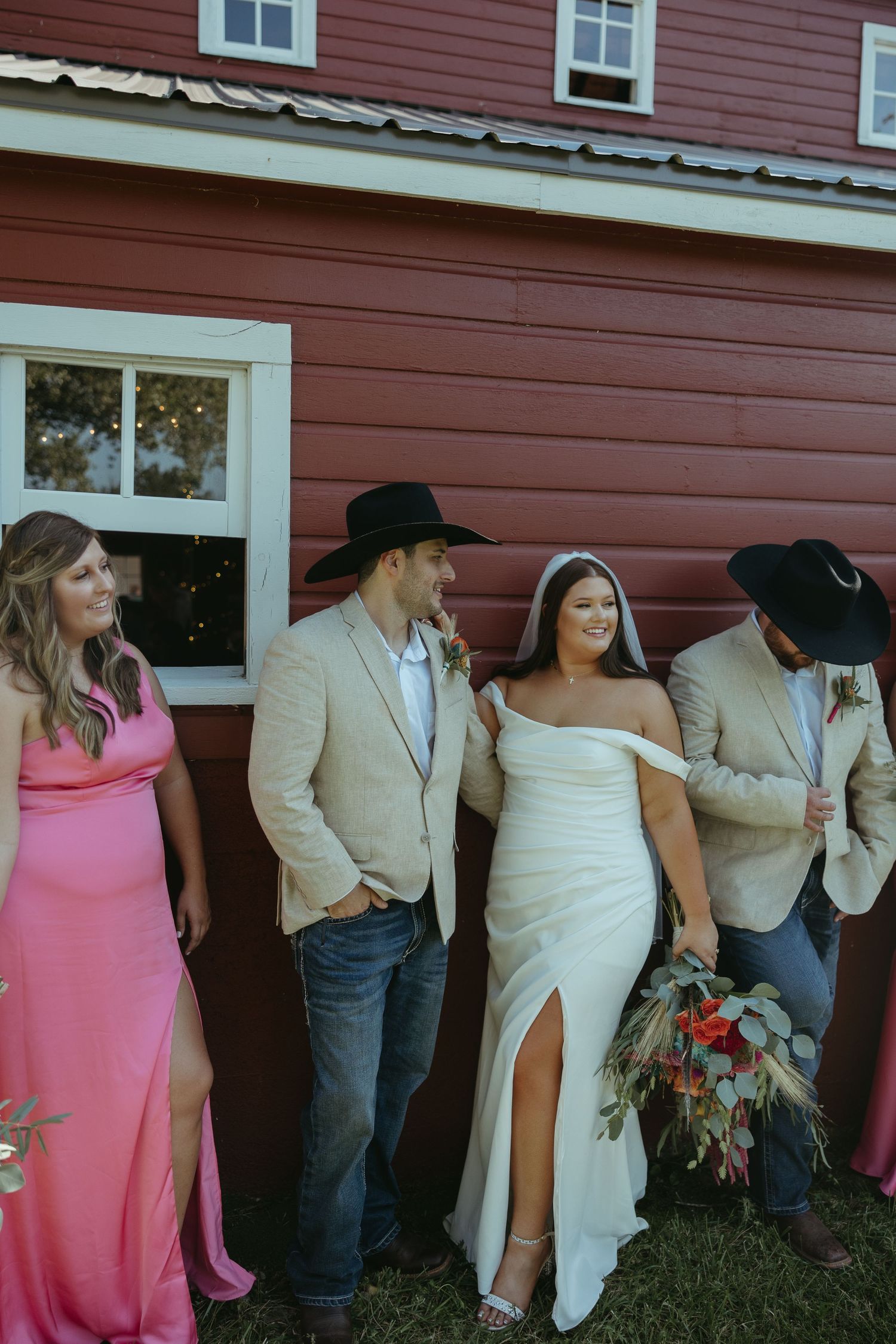 Wedding party poses together against a red barn wall during outdoor photo session.