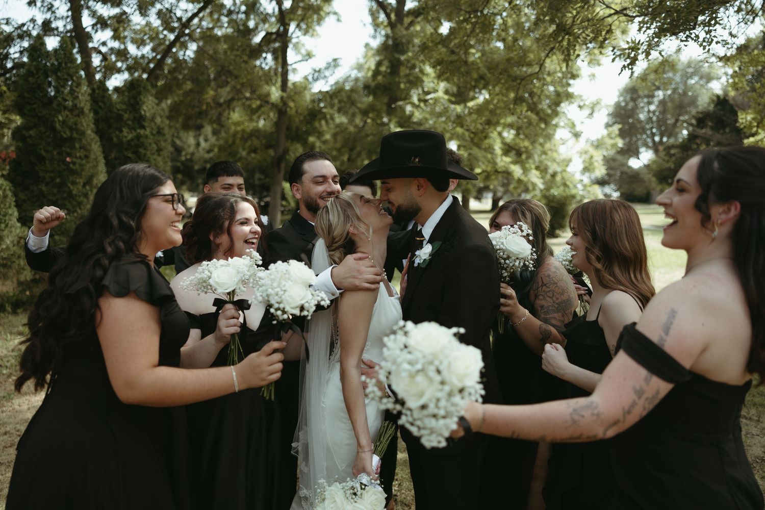 Wedding party celebrates joyfully outdoors with white floral arrangements in the background.