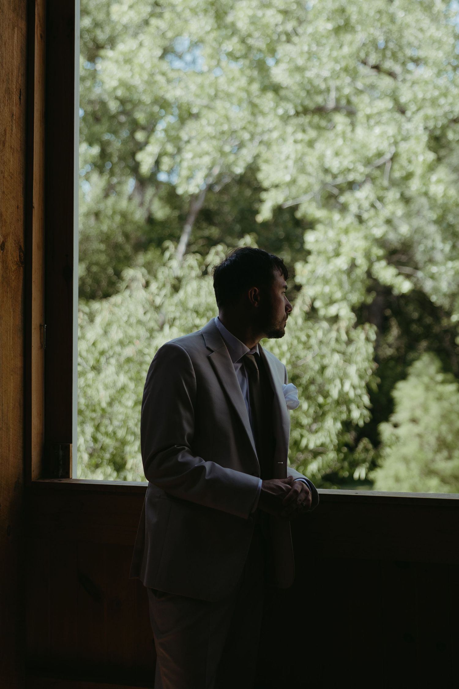 Silhouetted figure stands by window in dark room creating dramatic lighting.