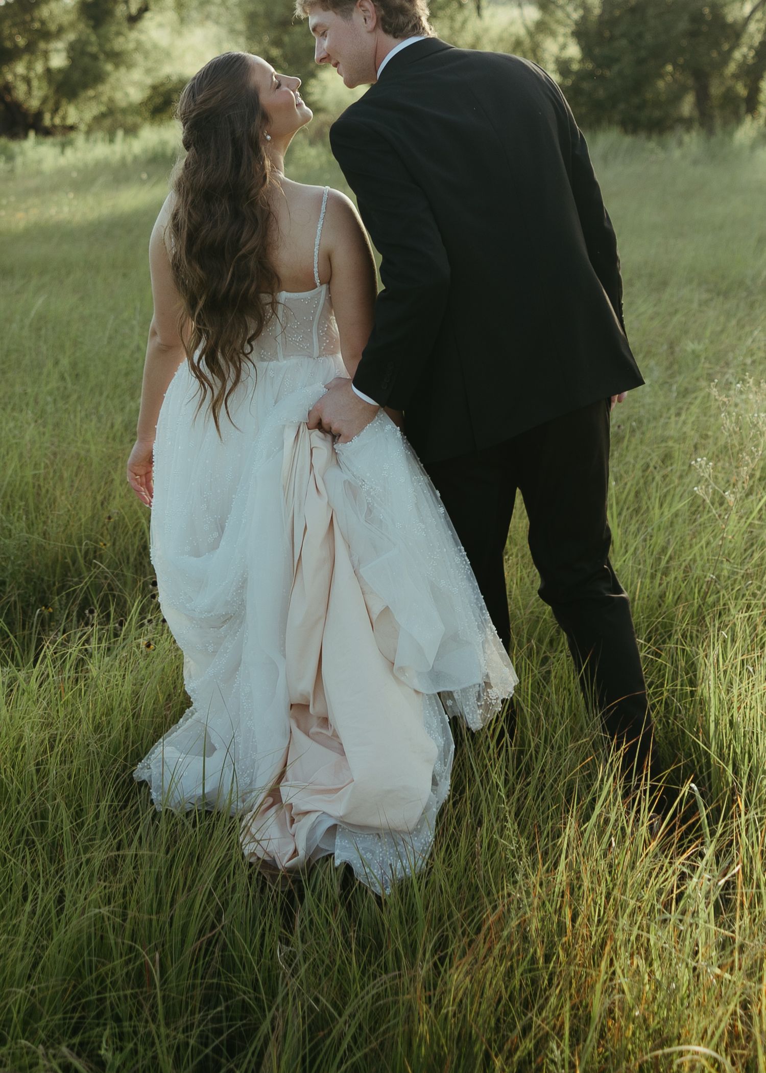 Romantic moment captured in tall grass with flowing white wedding dress.