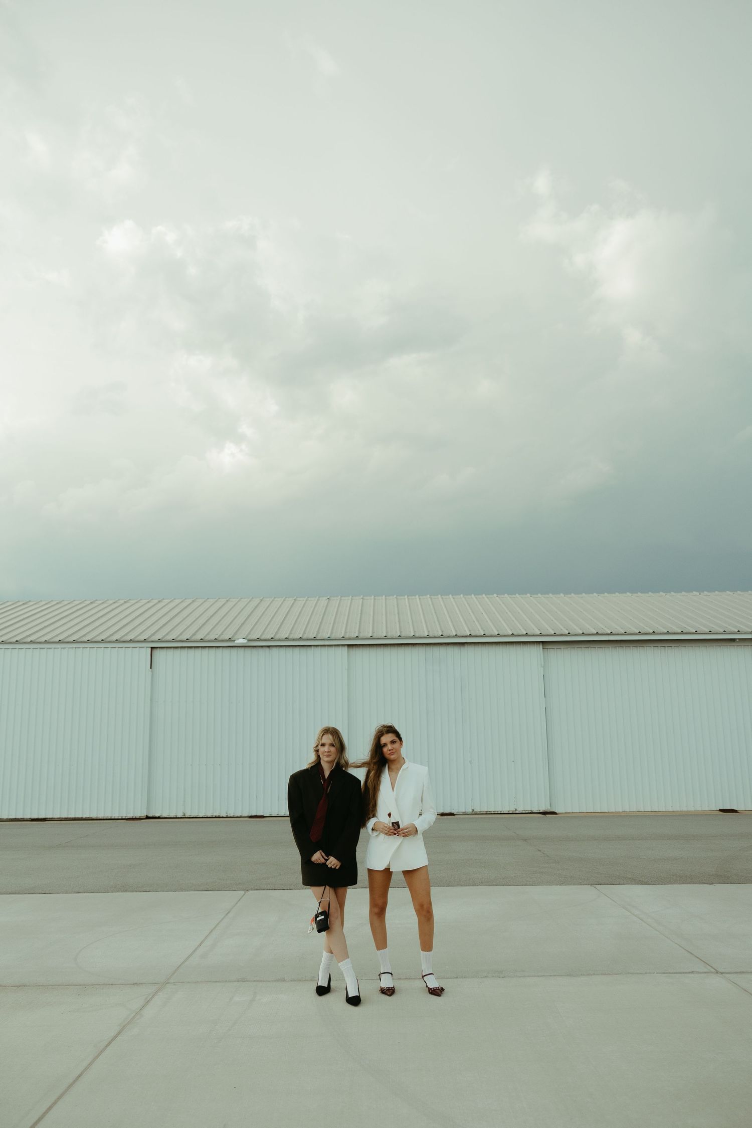 Two people standing against industrial backdrop on empty airfield.