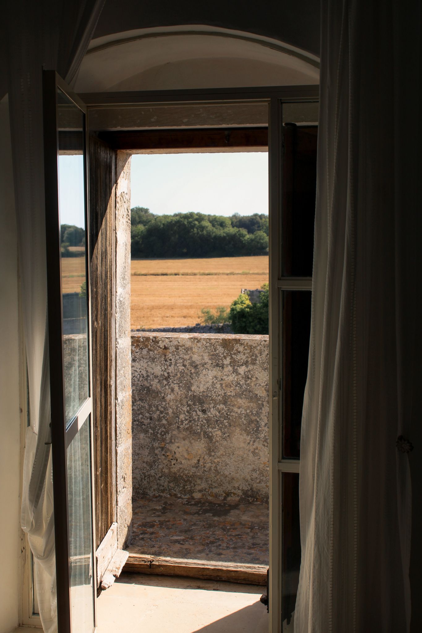 Boutique hotel room opening onto the Puglia countryside with flowing curtains and golden morning light