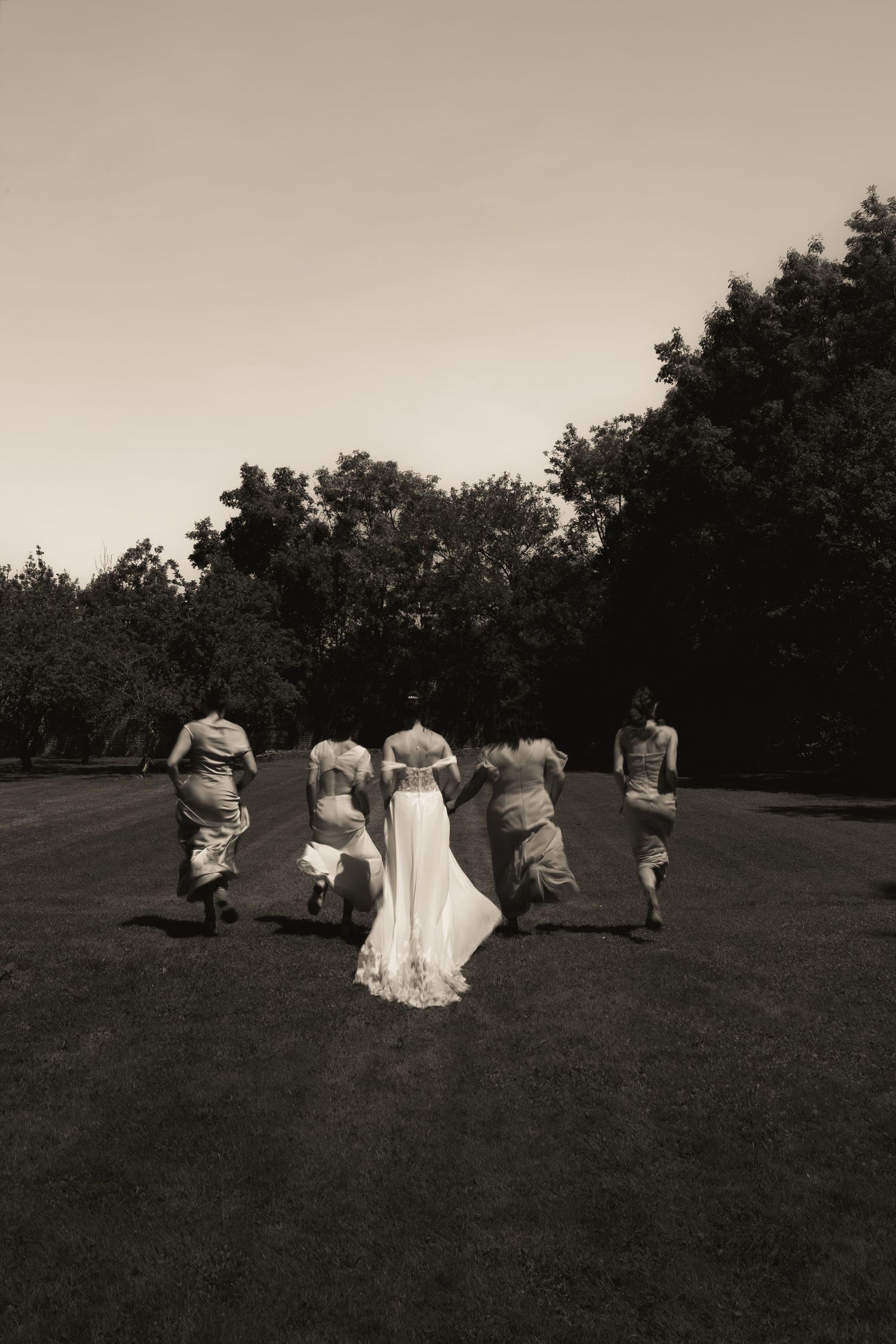 Black and white photograph of the bride and her bridesmaids running through the garden of the wedding venue