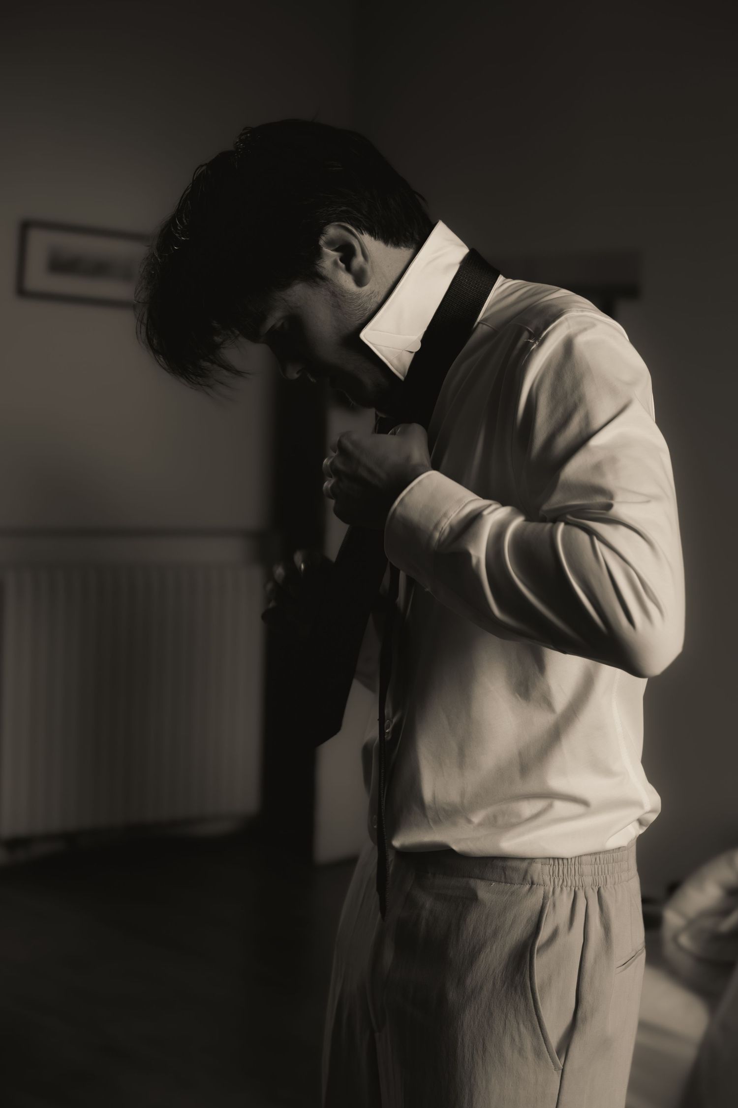 Groomsman's brother adjusting his tie before the wedding, captured in timeless black and white photography.