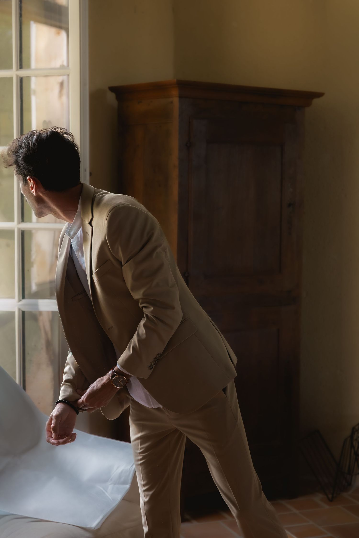 Groomsman getting ready before the wedding and looking through the window, captured in an editorial style.
