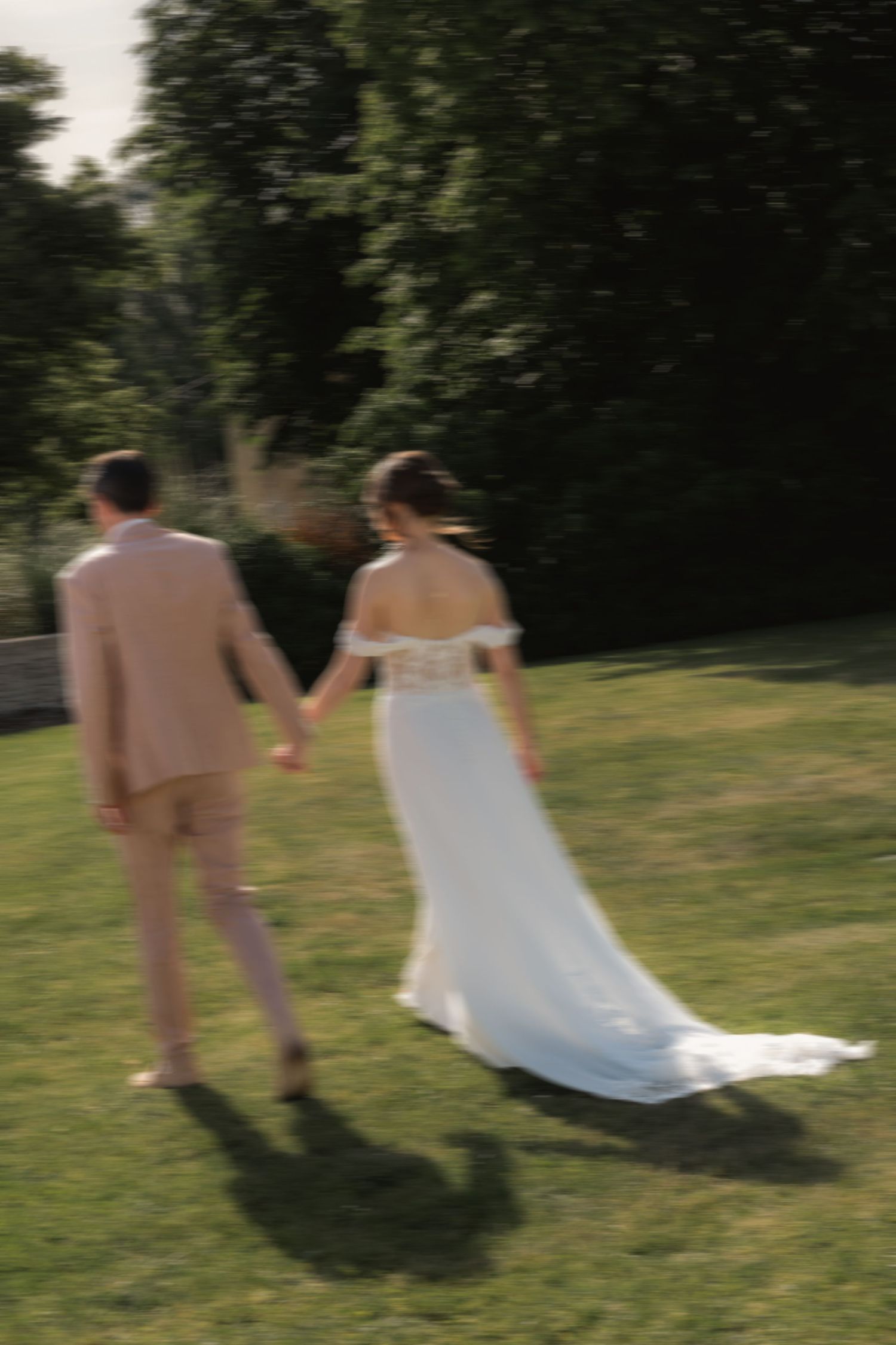 Bride and groom holding hands while walking through a garden with artistic motion blur