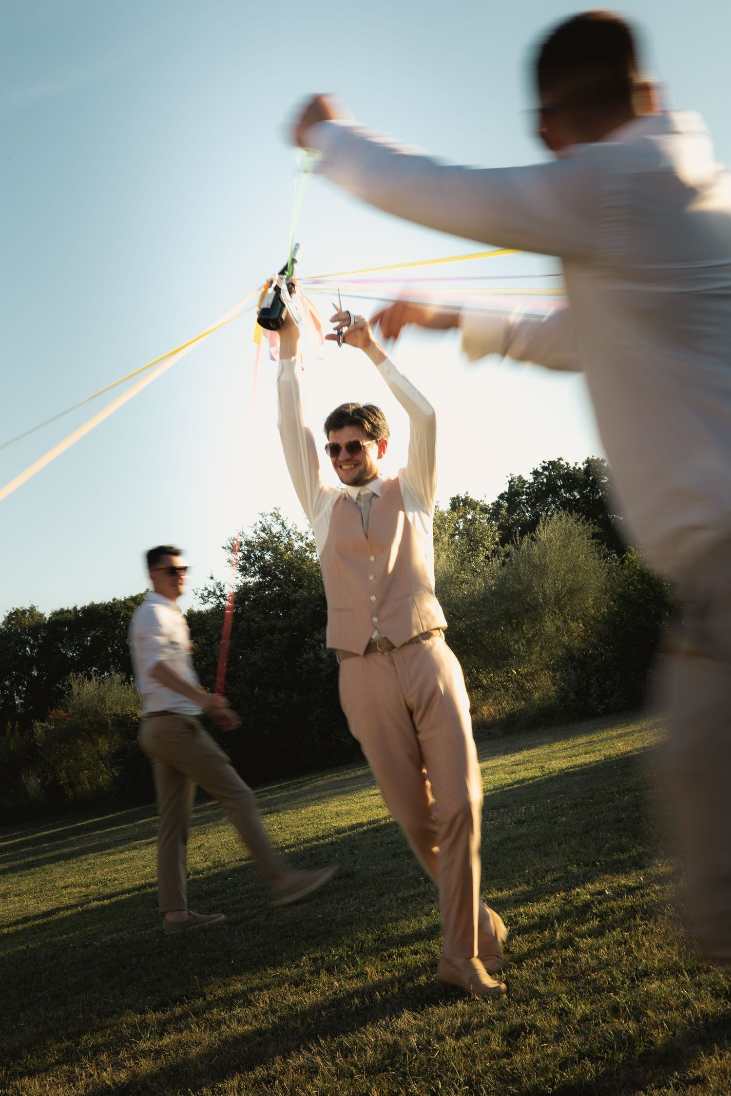 Groom cutting ribbons around a wine bottle surrounded by his friends during the wedding celebration