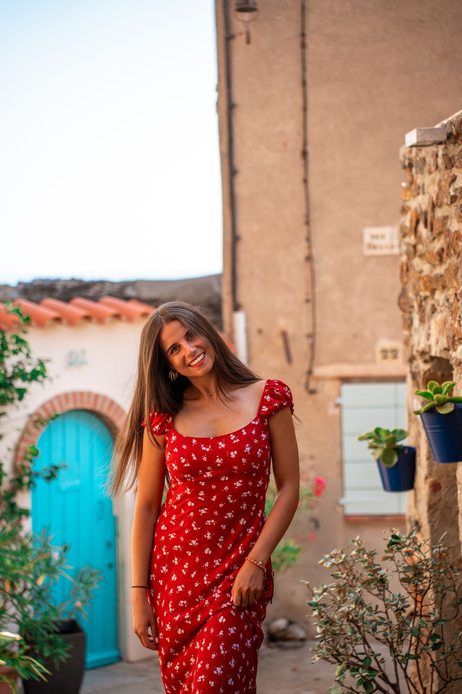 Portrait of a young woman wearing a red dress in a summer village, warm sunlight, soft colors and cinematic atmosphere.