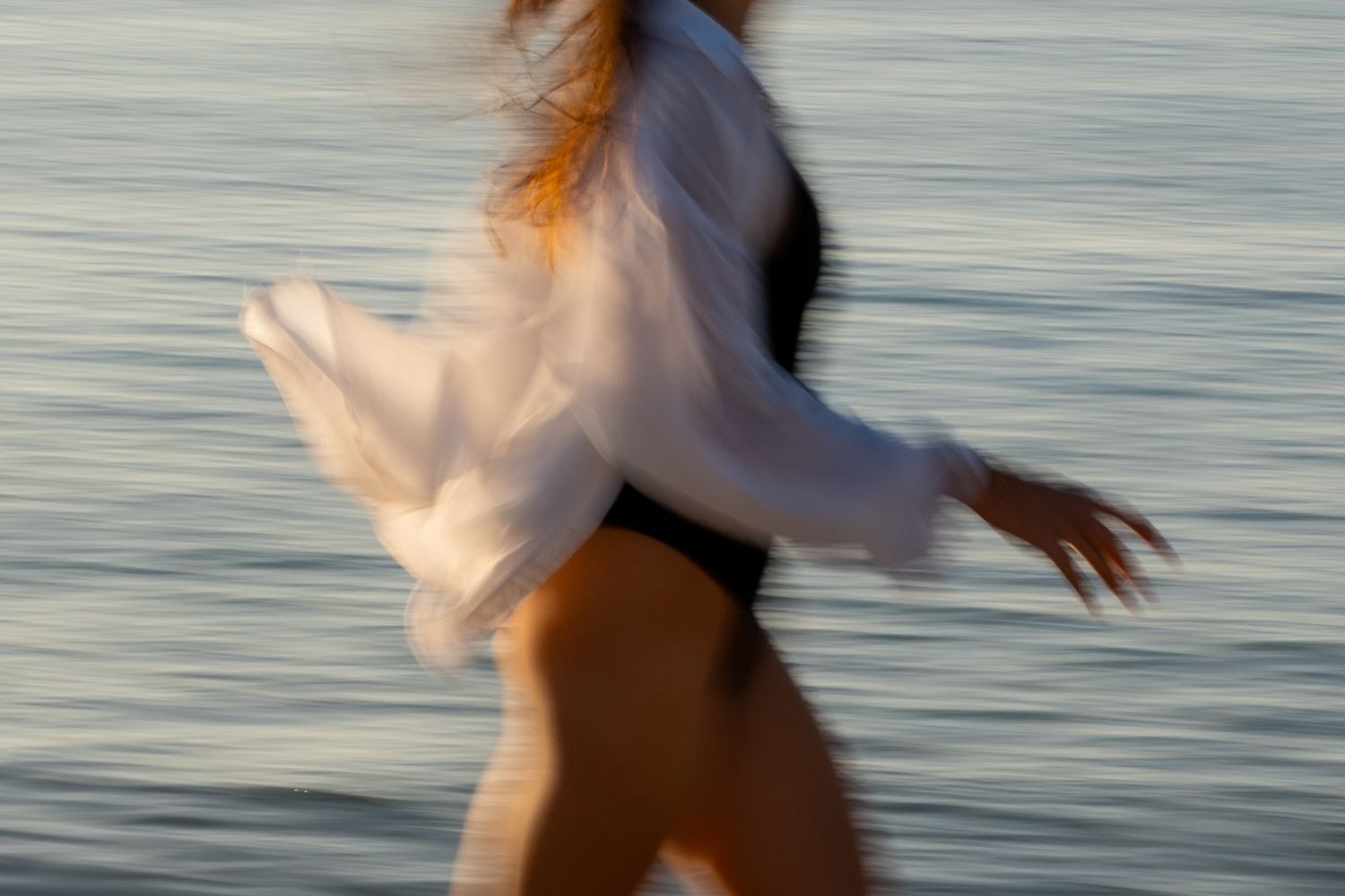 Portrait of a woman in movement on the beach in warm natural light, with ocean and soft tones creating a cinematic mood.