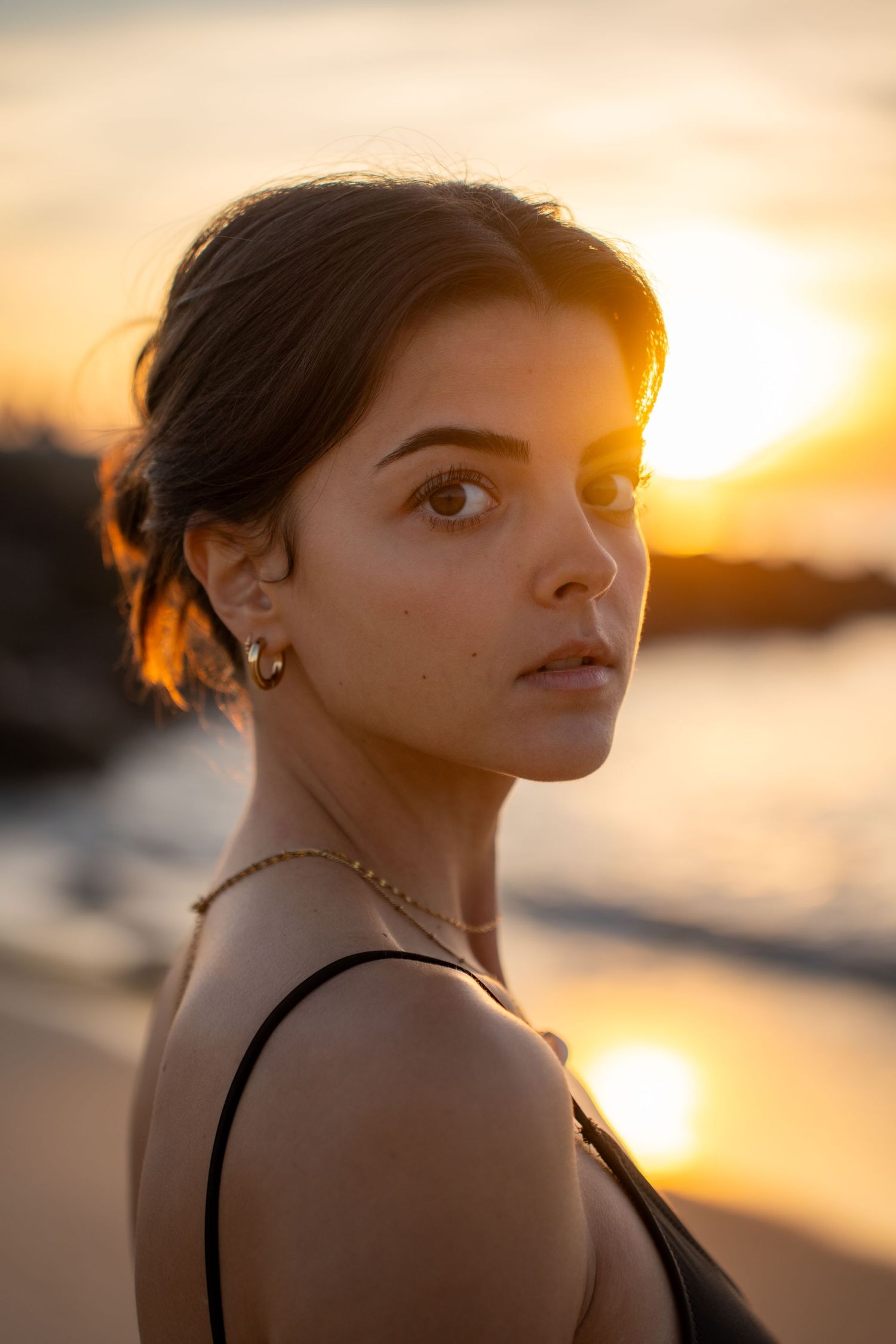 Portrait of a woman on the beach in warm natural light, with ocean and soft tones creating a cinematic mood.