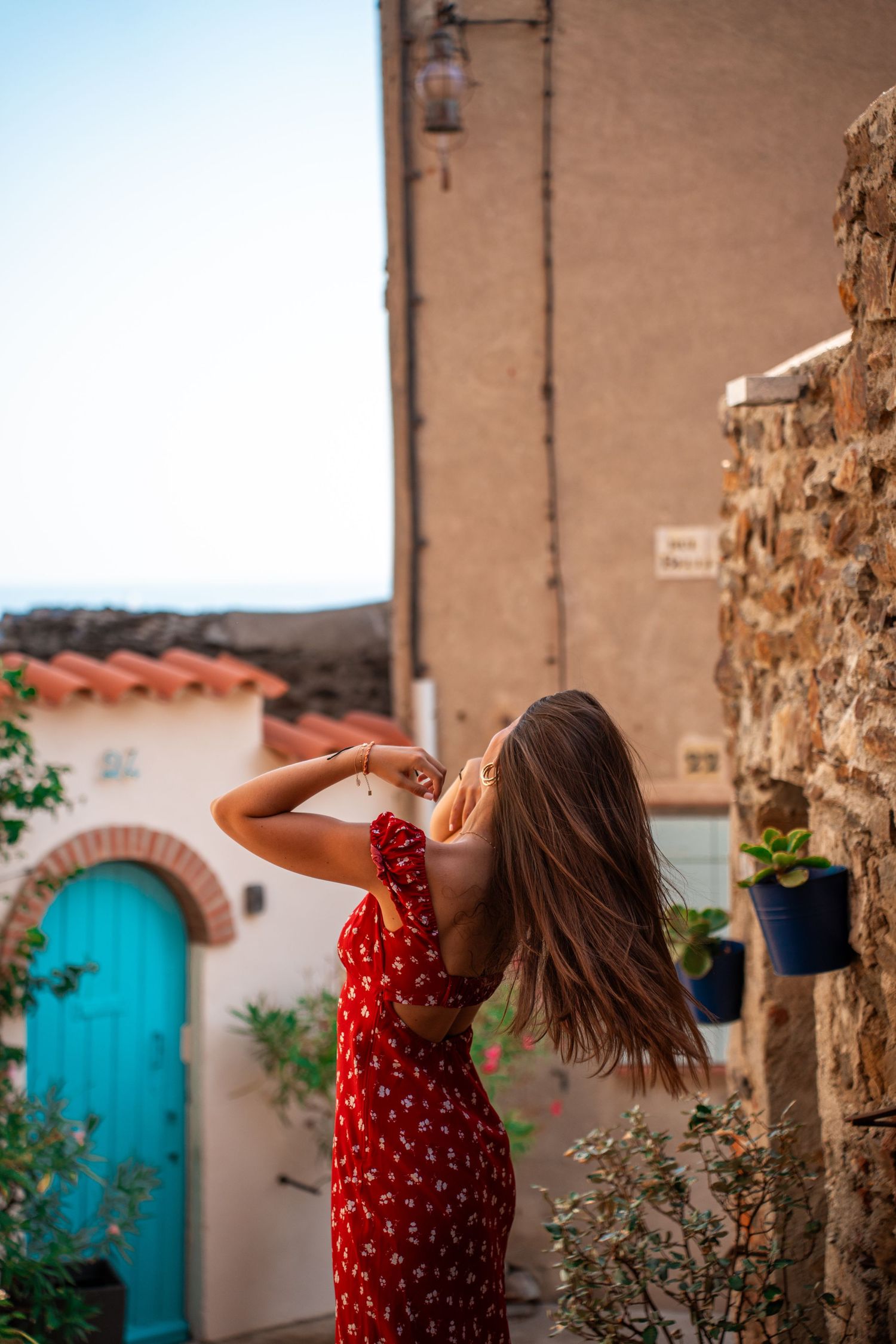 Portrait of a young woman wearing a red dress in a summer village, warm sunlight, soft colors and cinematic atmosphere.