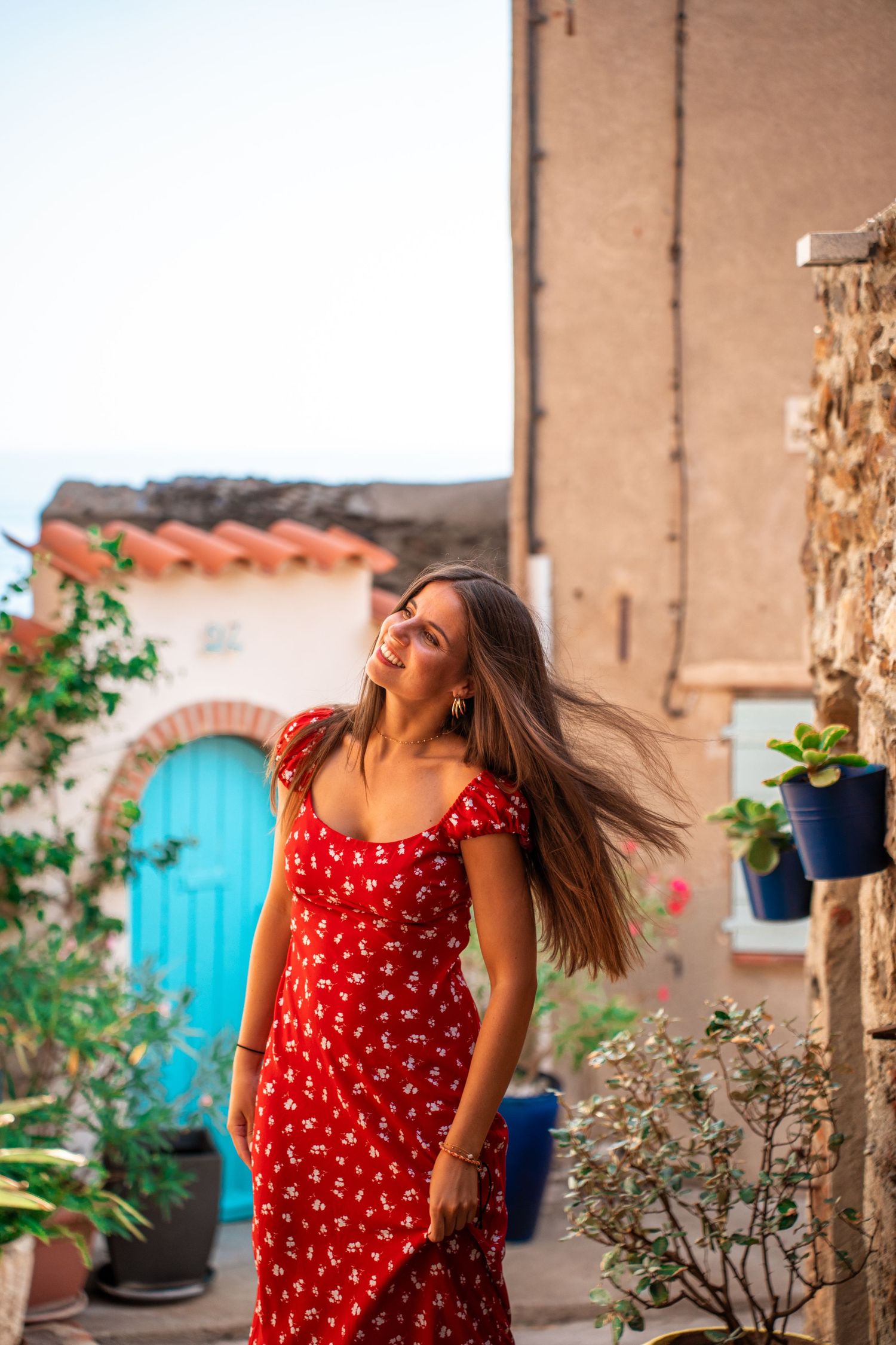 Portrait of a young woman wearing a red dress in a summer village, warm sunlight, soft colors and cinematic atmosphere.
