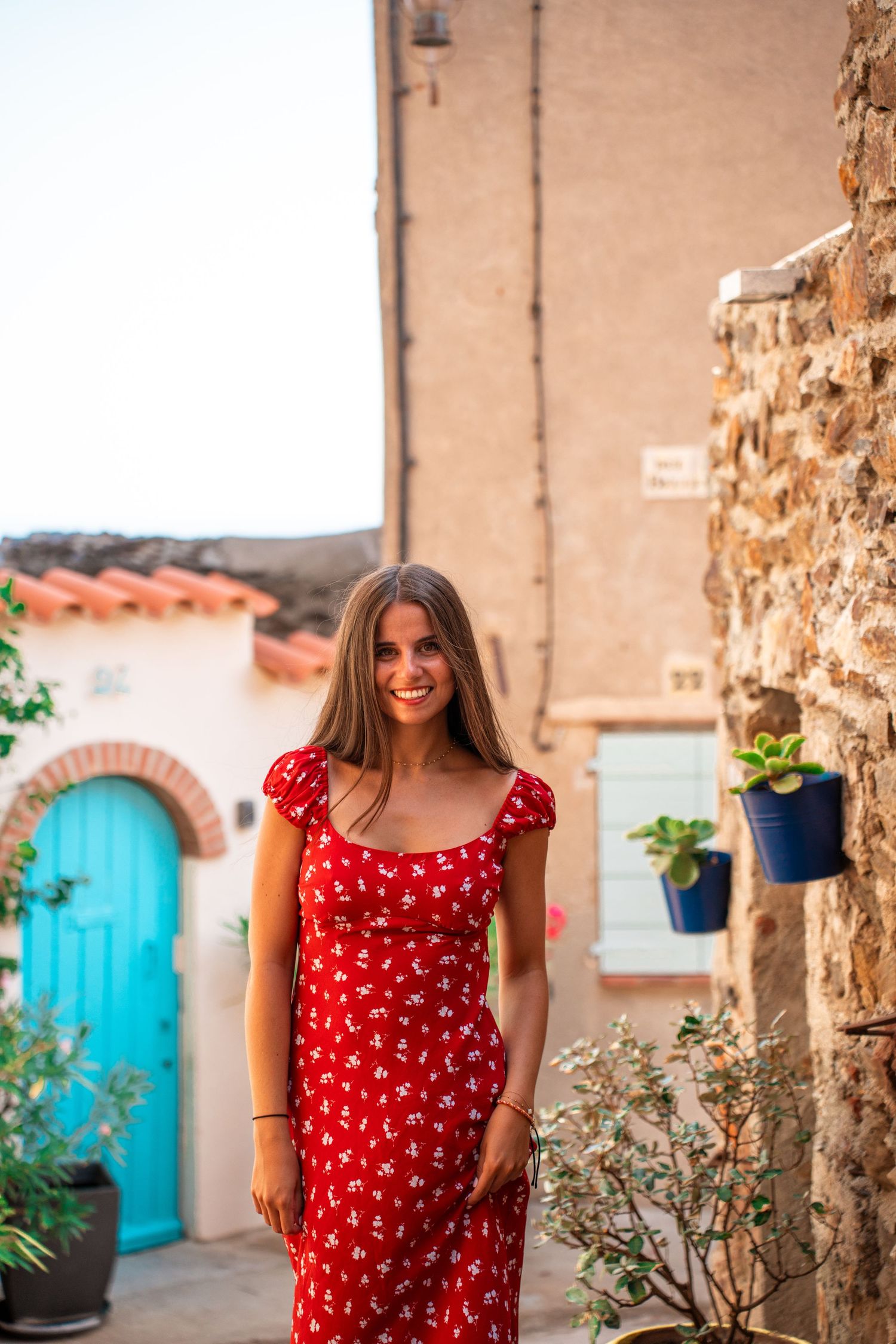 Portrait of a young woman wearing a red dress in a summer village, warm sunlight, soft colors and cinematic atmosphere.