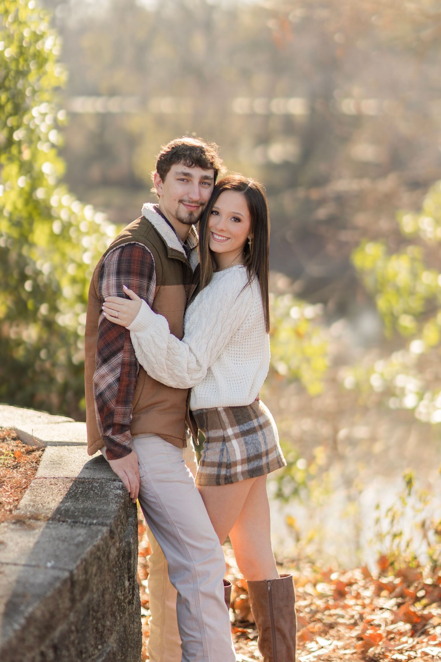 Couple embraces while sitting on fallen tree trunk during autumn photoshoot.