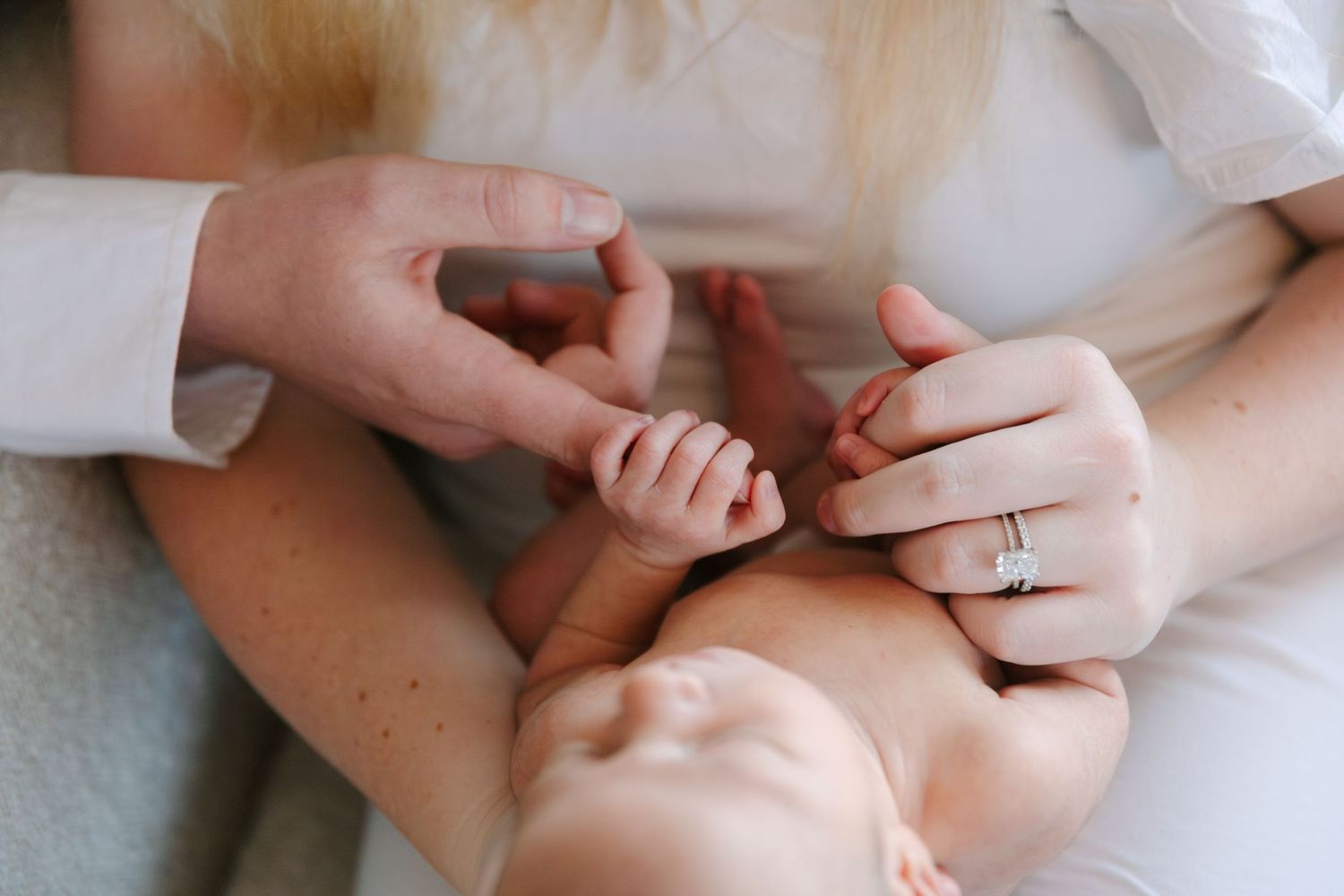 Close-up of newborn baby holding parent's finger while resting on mother's lap, with wedding ring visible.