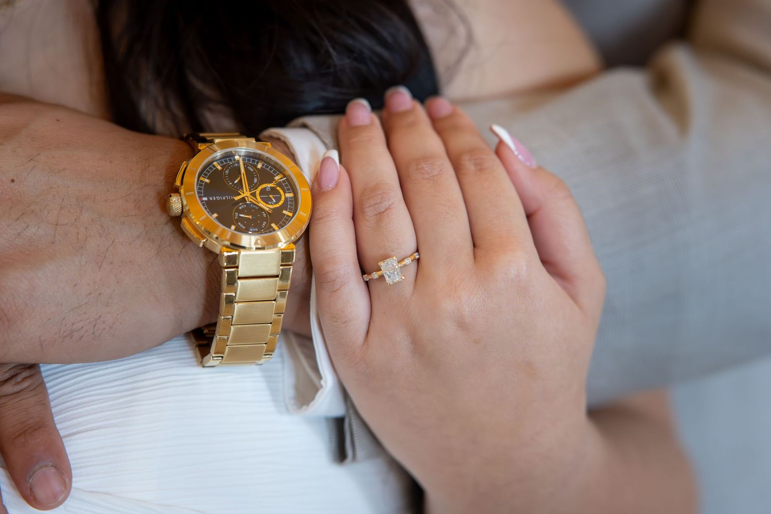 Close-up of a couple holding hands, woman wearing a diamond ring, man wearing a gold luxury watch.