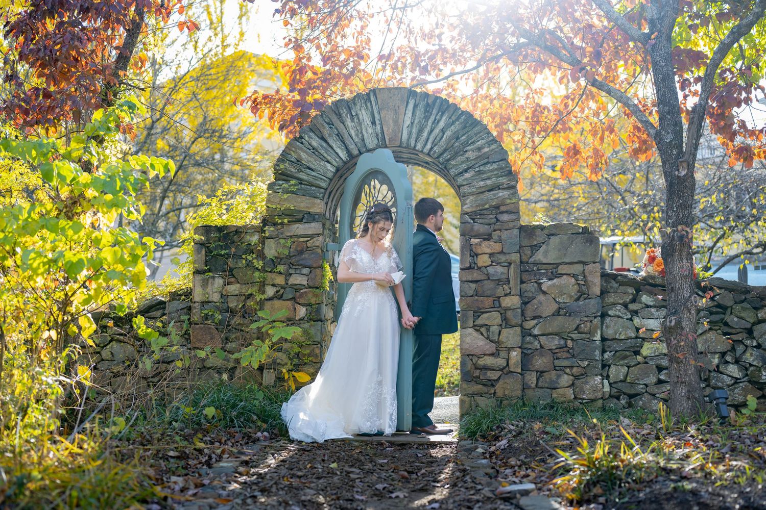 Couple shares romantic moments against stone walls surrounded by vibrant autumn foliage in an outdoor wedding setting.