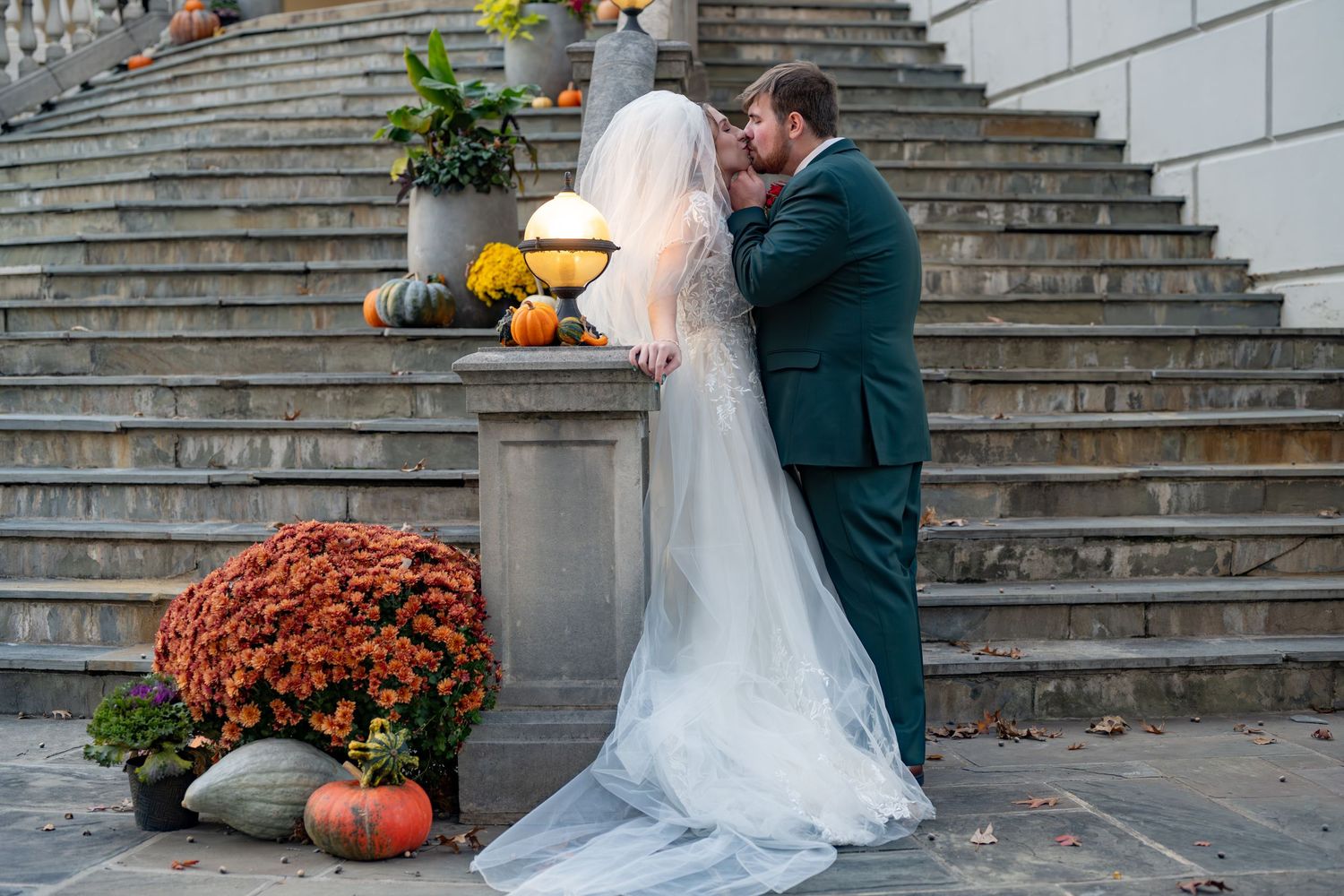 A romantic autumn wedding scene on stone steps decorated with orange mums and pumpkins.