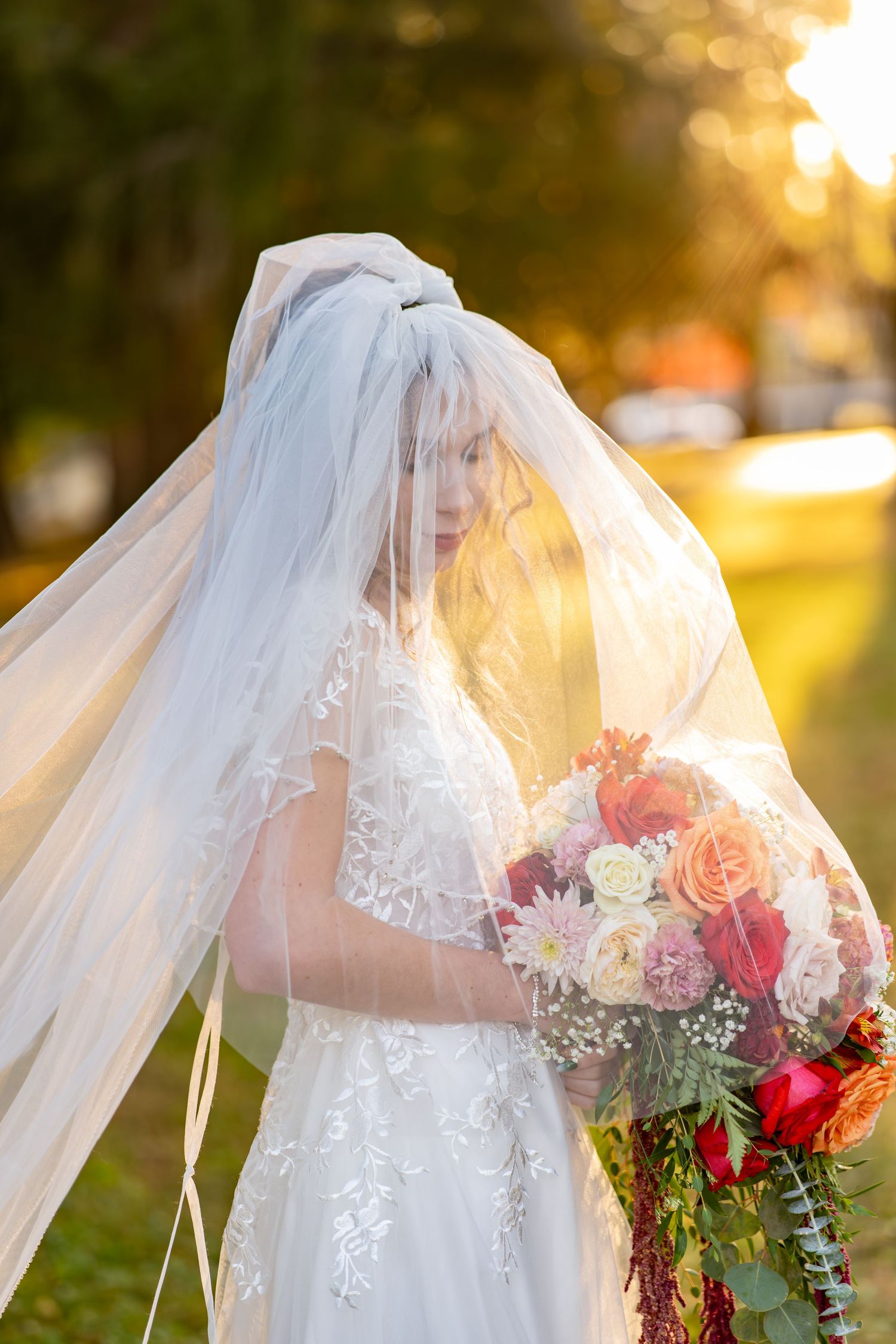 A flowing white wedding veil and colorful bouquet of roses and mixed flowers captured in golden sunset light.